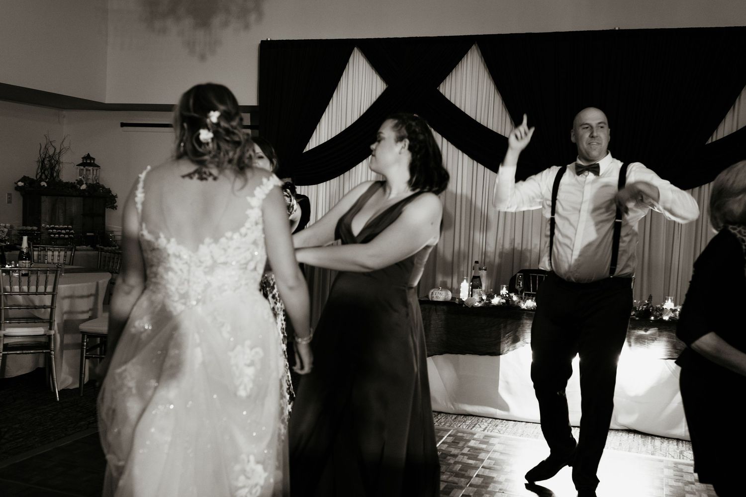 Bride and wedding guests dance joyfully on the reception dance floor in black and white photo.