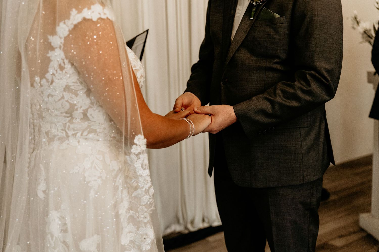 Close-up of bride and groom exchanging rings during wedding ceremony, bride wearing lace gown with veil.