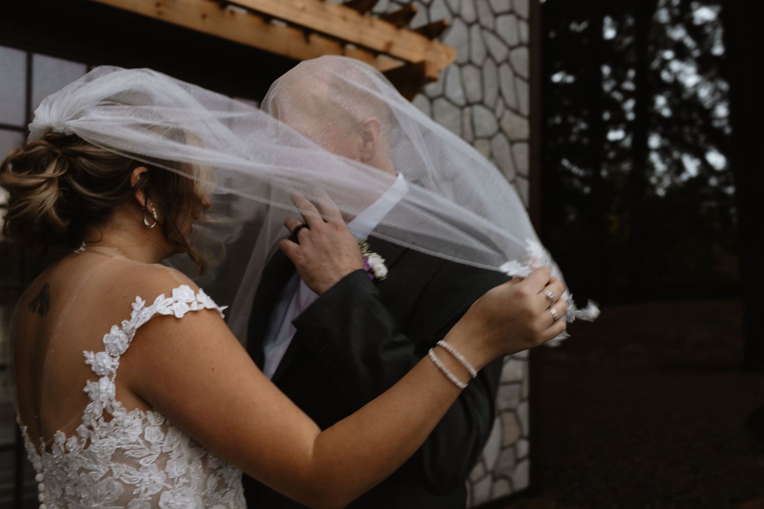 Bride and groom share a kiss under flowing wedding veil outdoors.