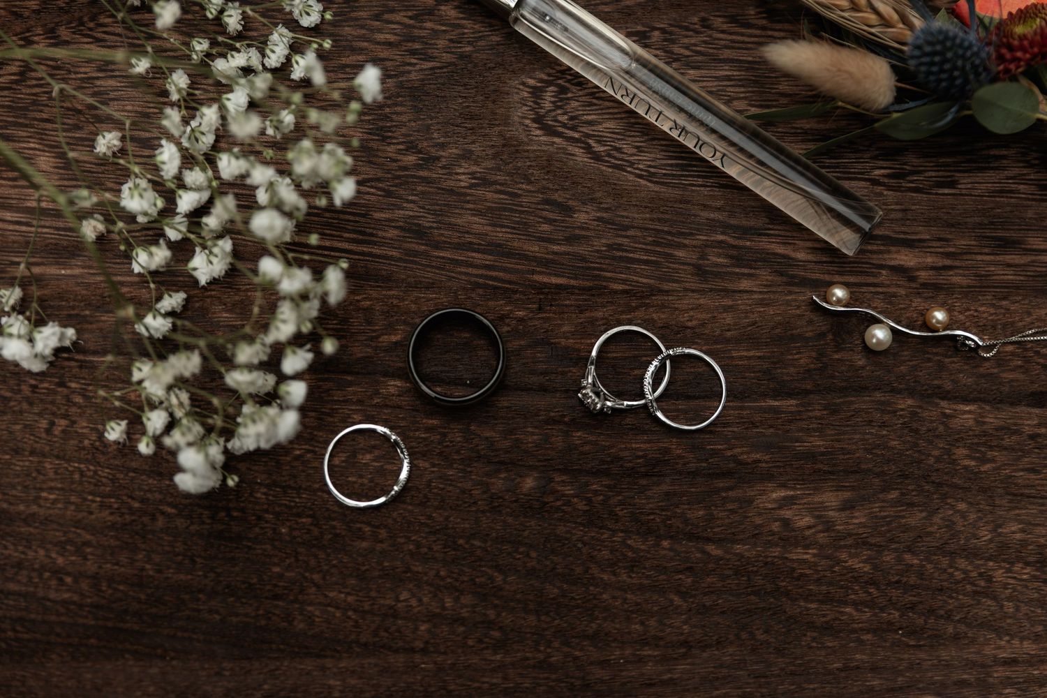 Wedding rings and jewelry arranged on a rustic wooden table with baby's breath flowers and elegant accessories.