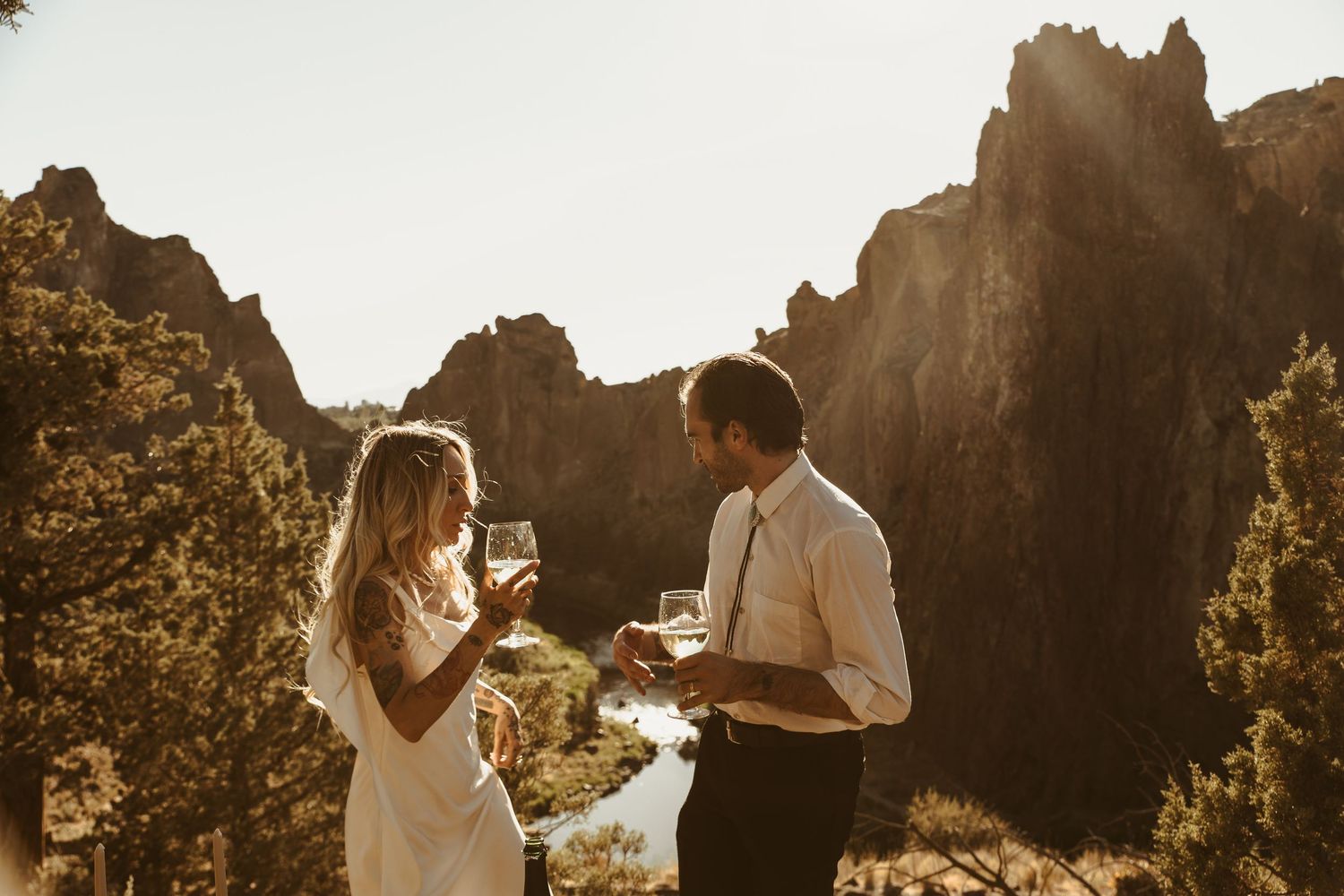 Bride and groom toasting with champagne at golden hour overlooking a stunning rocky canyon landscape.