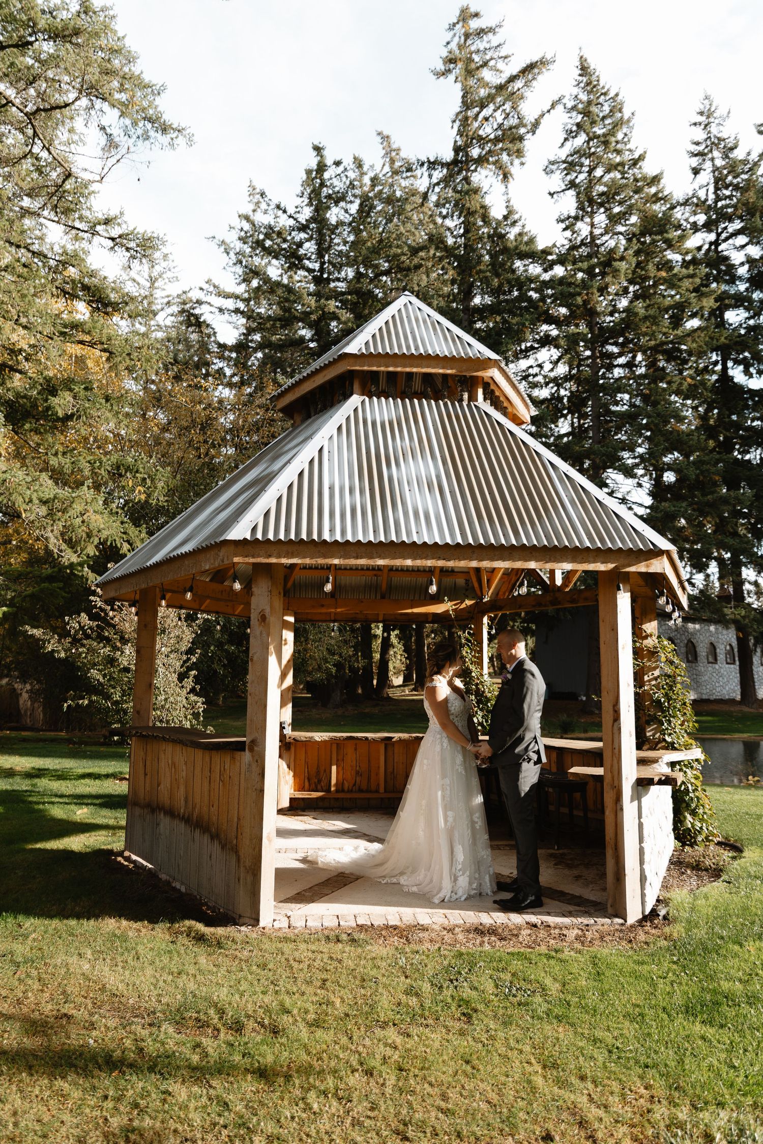 Bride and groom share intimate first look moment inside wooden gazebo surrounded by lush green lawn.