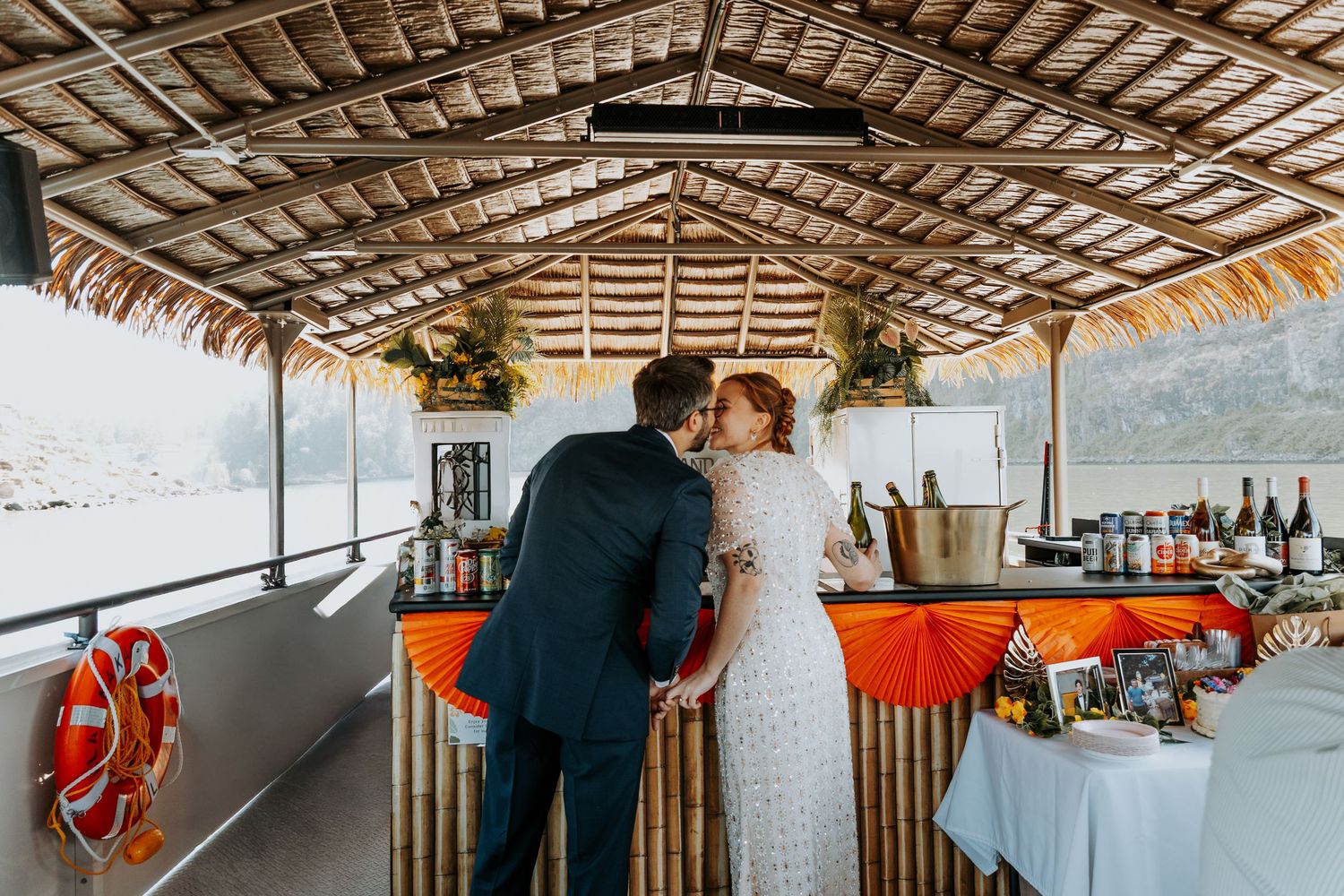 Couple sharing a romantic kiss at an outdoor waterfront bar decorated for a wedding celebration.