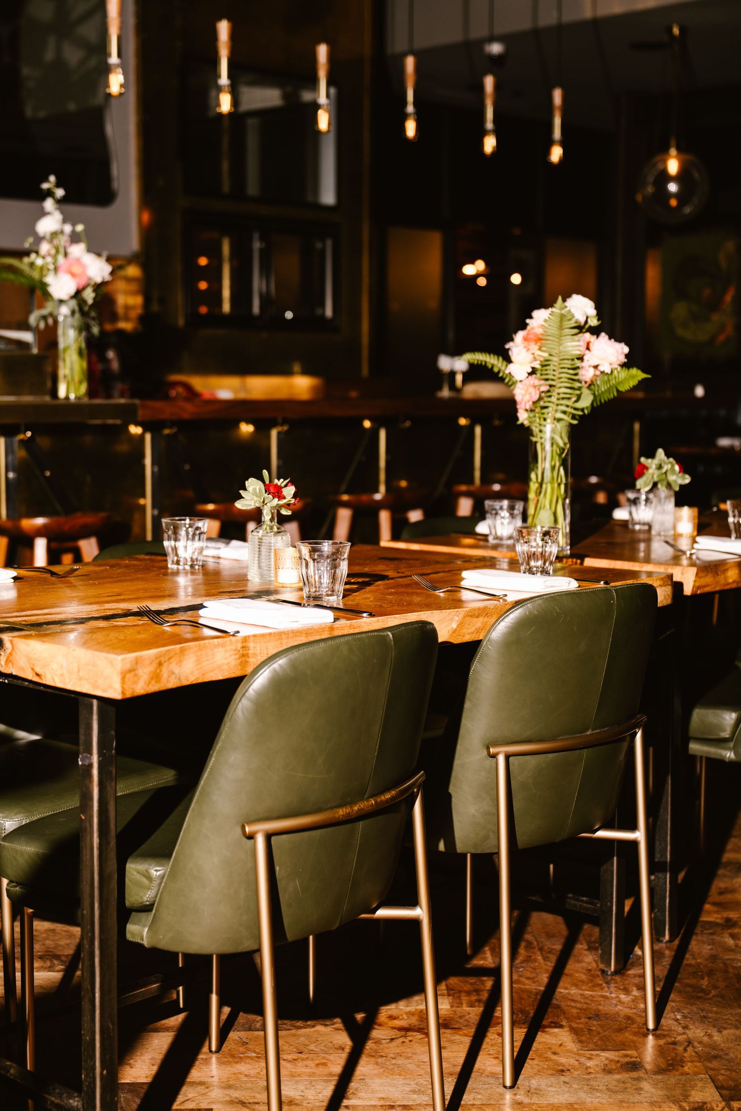 Elegant restaurant dining table with green leather chairs, floral centerpieces, and warm ambient lighting.