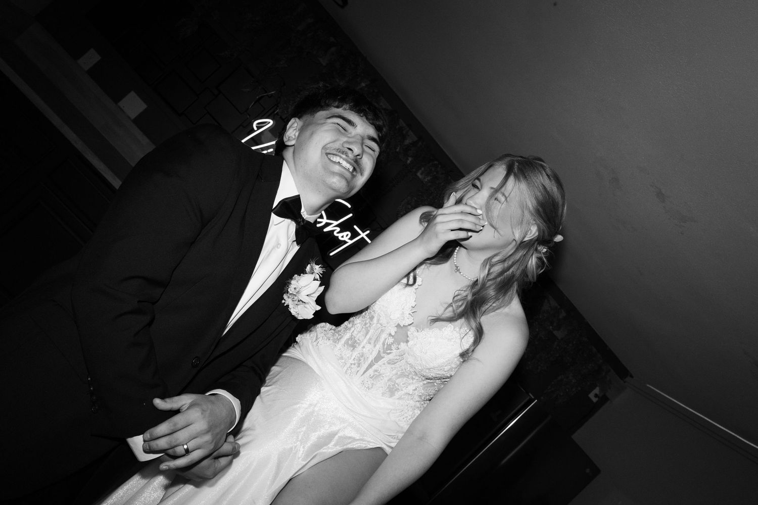 Black and white photo of a couple in formal wear laughing joyfully, man in tuxedo and woman in white dress.