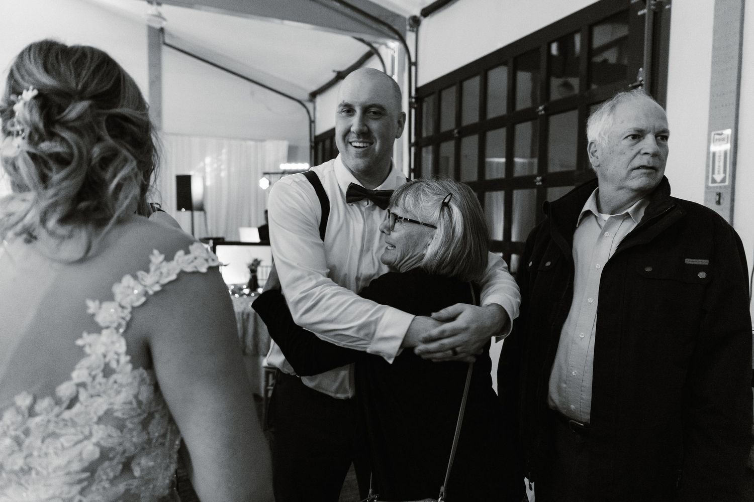 Groom in bow tie and suspenders greets elderly guests warmly at the wedding reception.