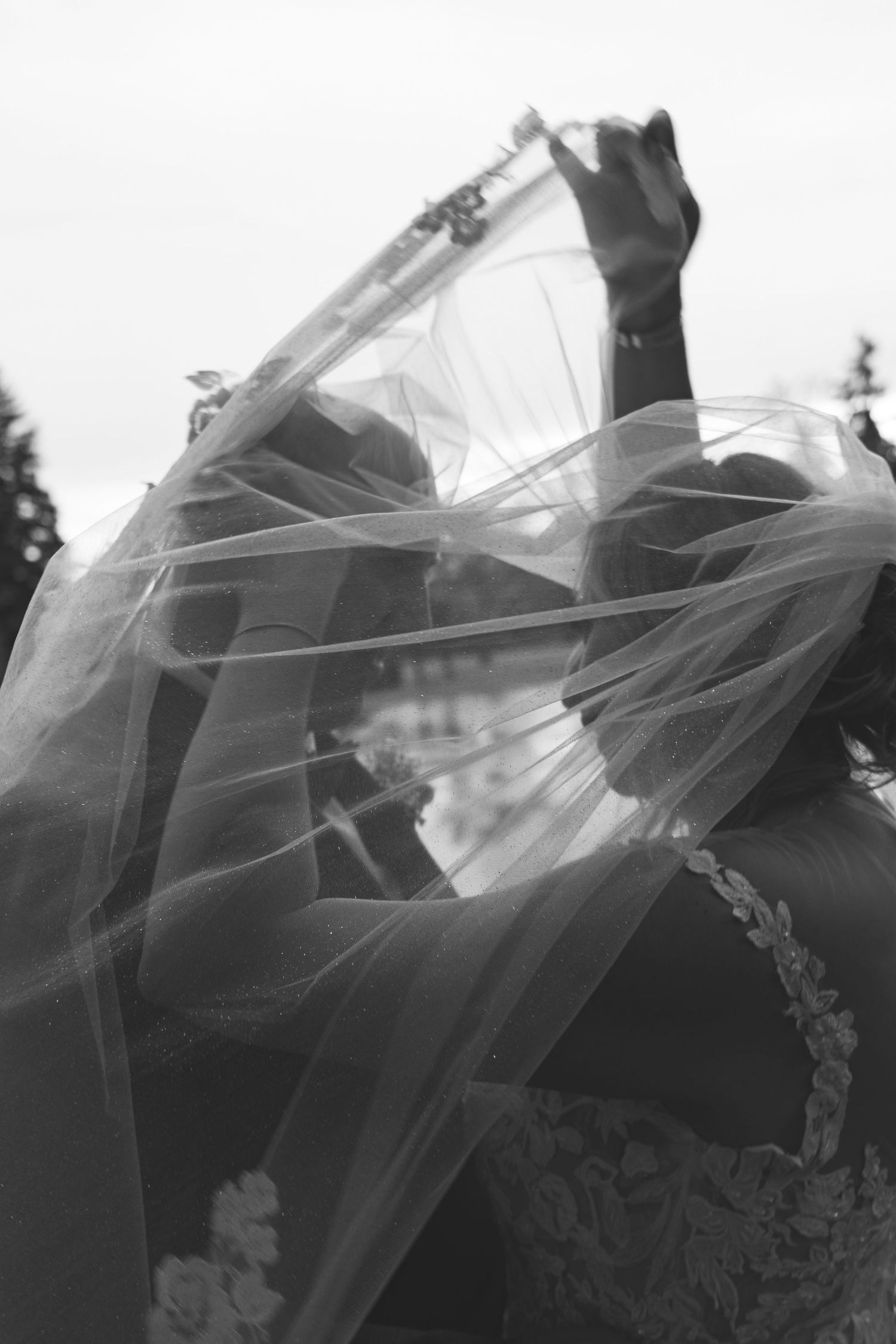 Black and white photo of a bride's veil blowing in the wind during an outdoor wedding ceremony.