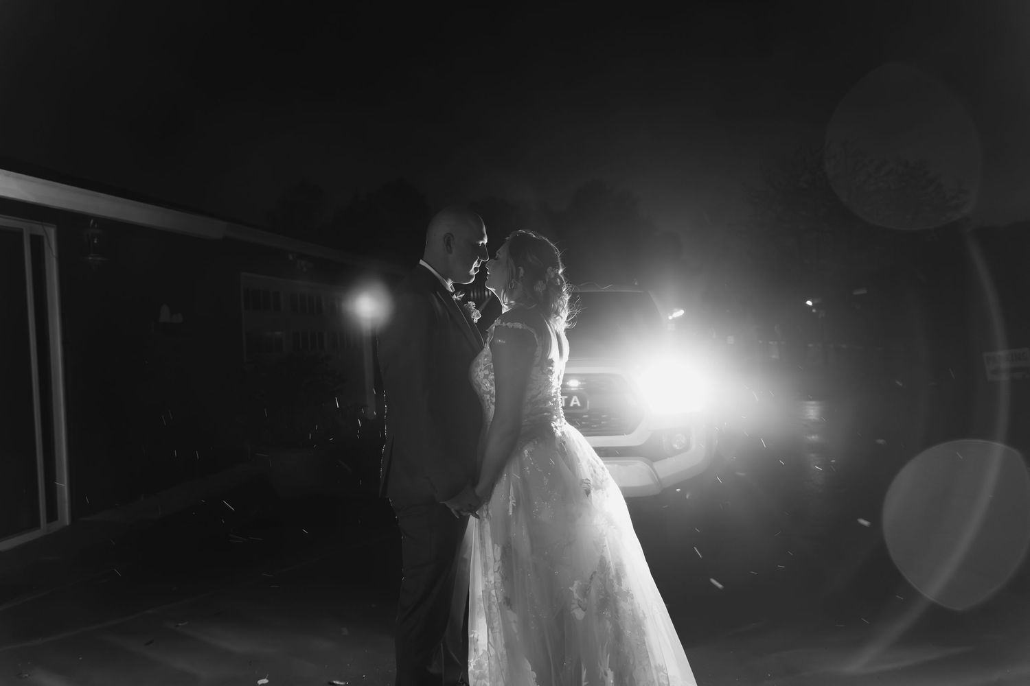 Bride and groom share a romantic dance outdoors at night with dramatic backlighting.