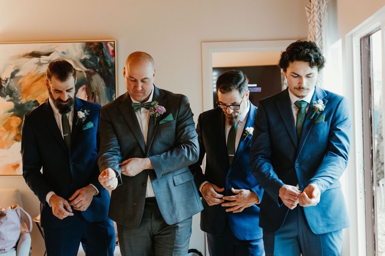 Four groomsmen in blue suits adjusting cufflinks and boutonnieres while getting ready for a wedding ceremony.
