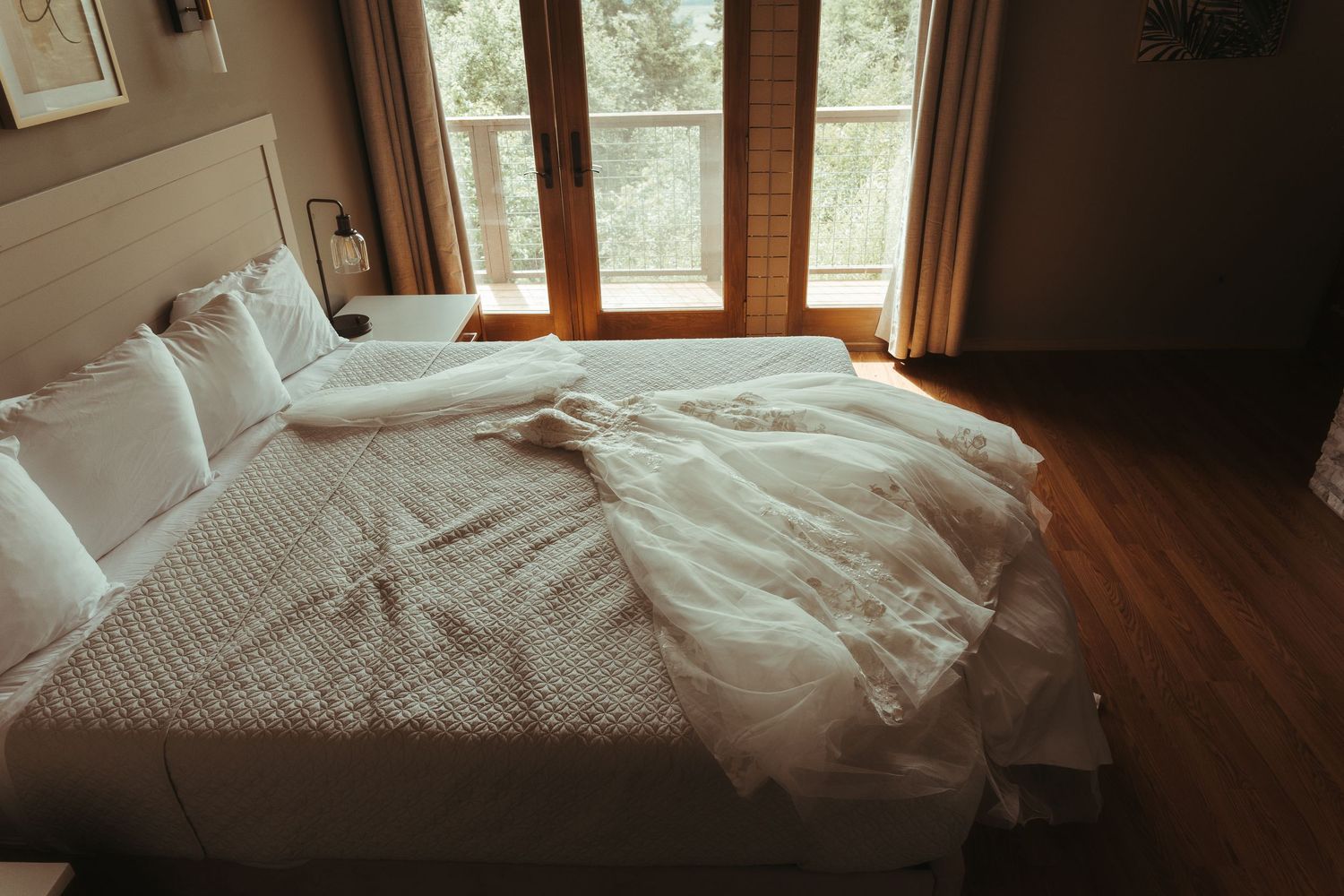 White wedding dress laid out on a large bed with white pillows in a cozy wood-paneled room with natural light.