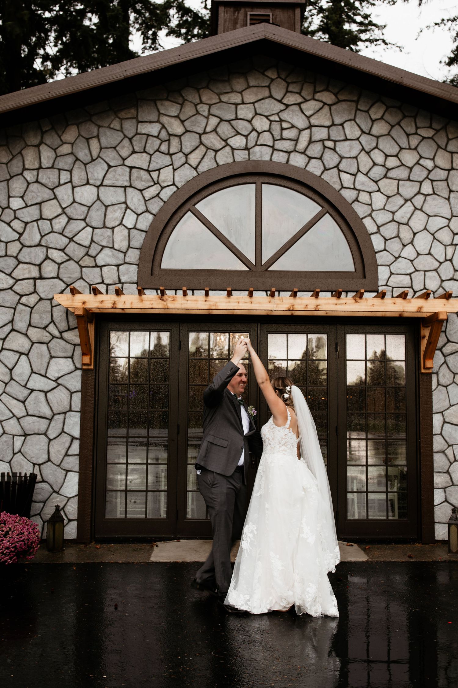 Bride and groom dancing in the rain outside a stone wedding venue.