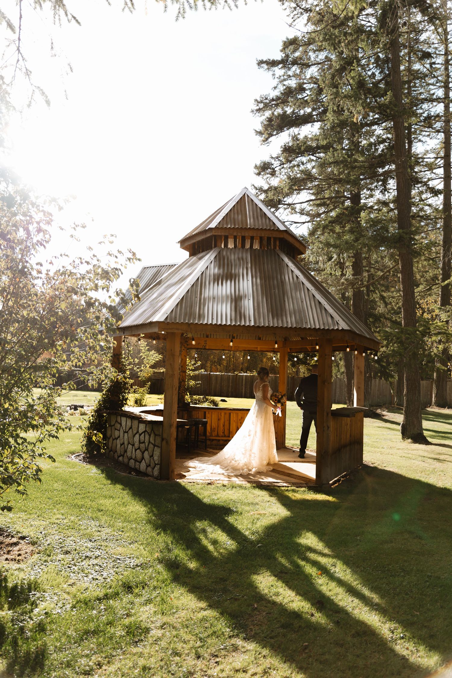 Bride and groom share first look moment inside charming wooden gazebo surrounded by tall pine trees.