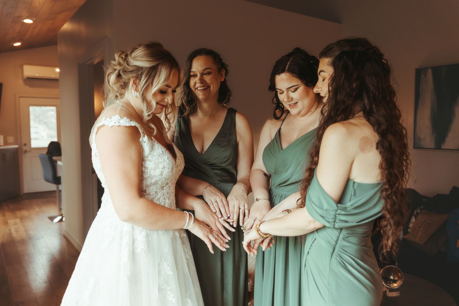 Bride and three bridesmaids in green dresses sharing a joyful moment looking at hands.
