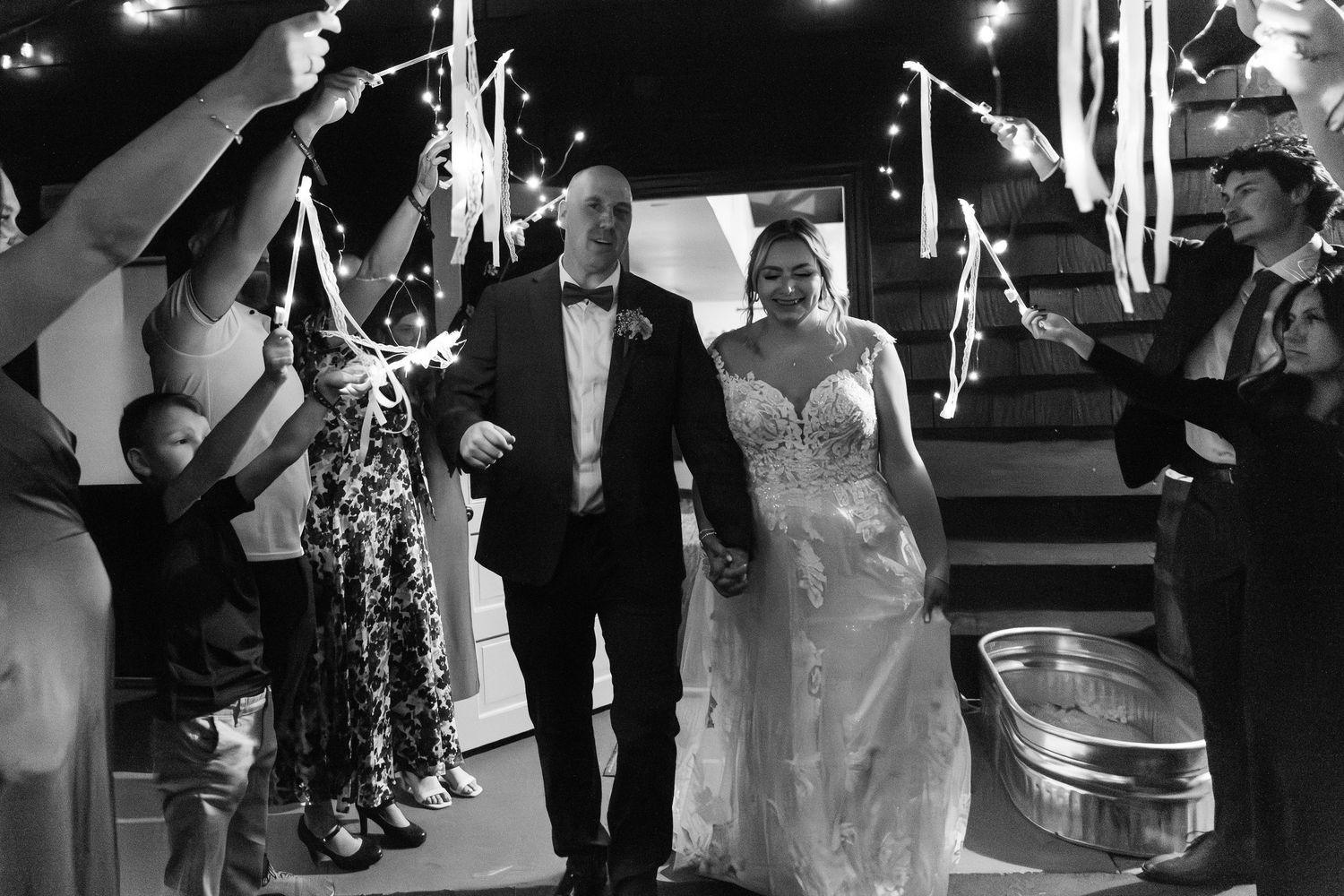 Bride and groom exit wedding reception through a sparkler send-off tunnel with cheering guests.