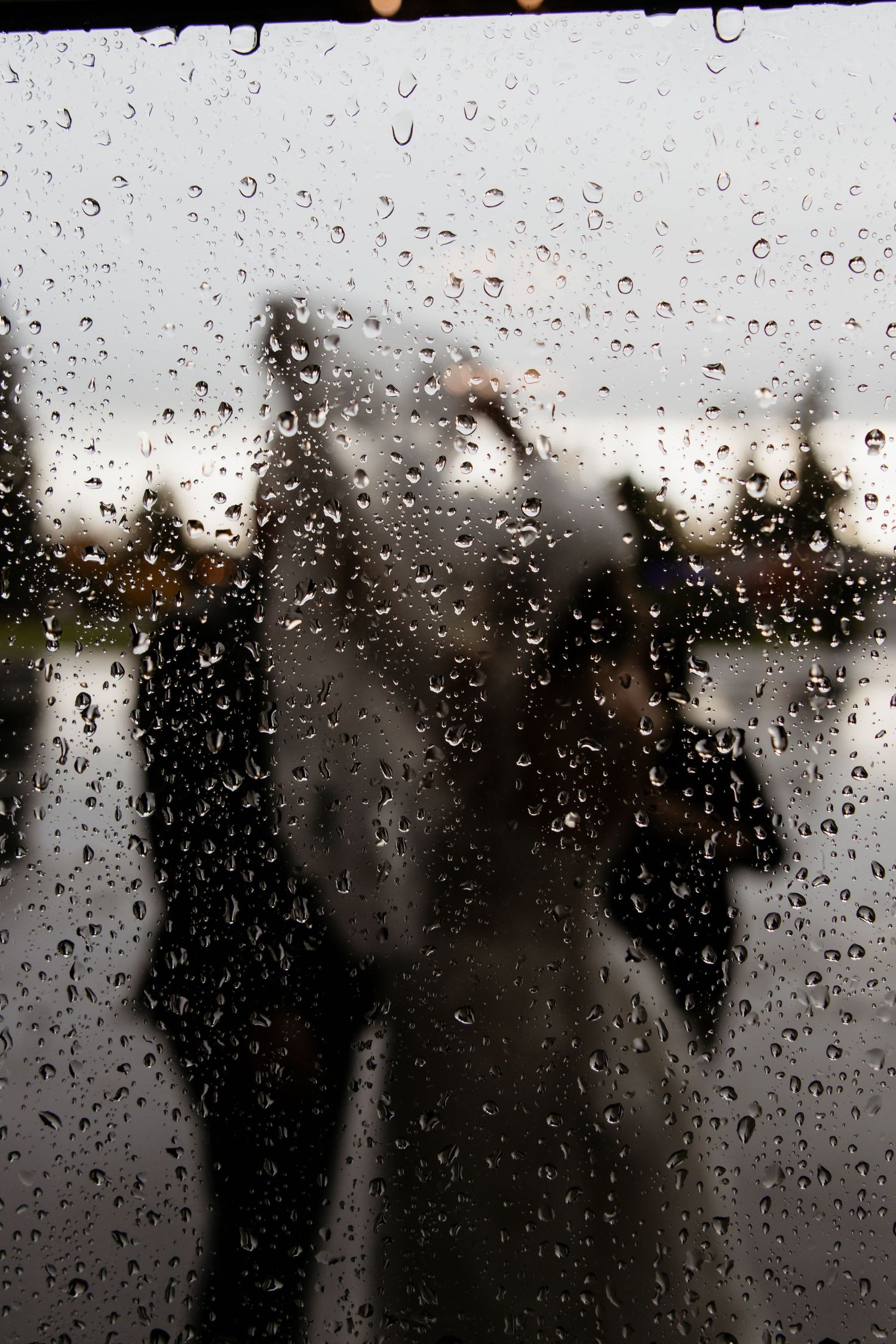 Rainy day wedding viewed through a rain-covered window with blurred silhouettes of guests outside.