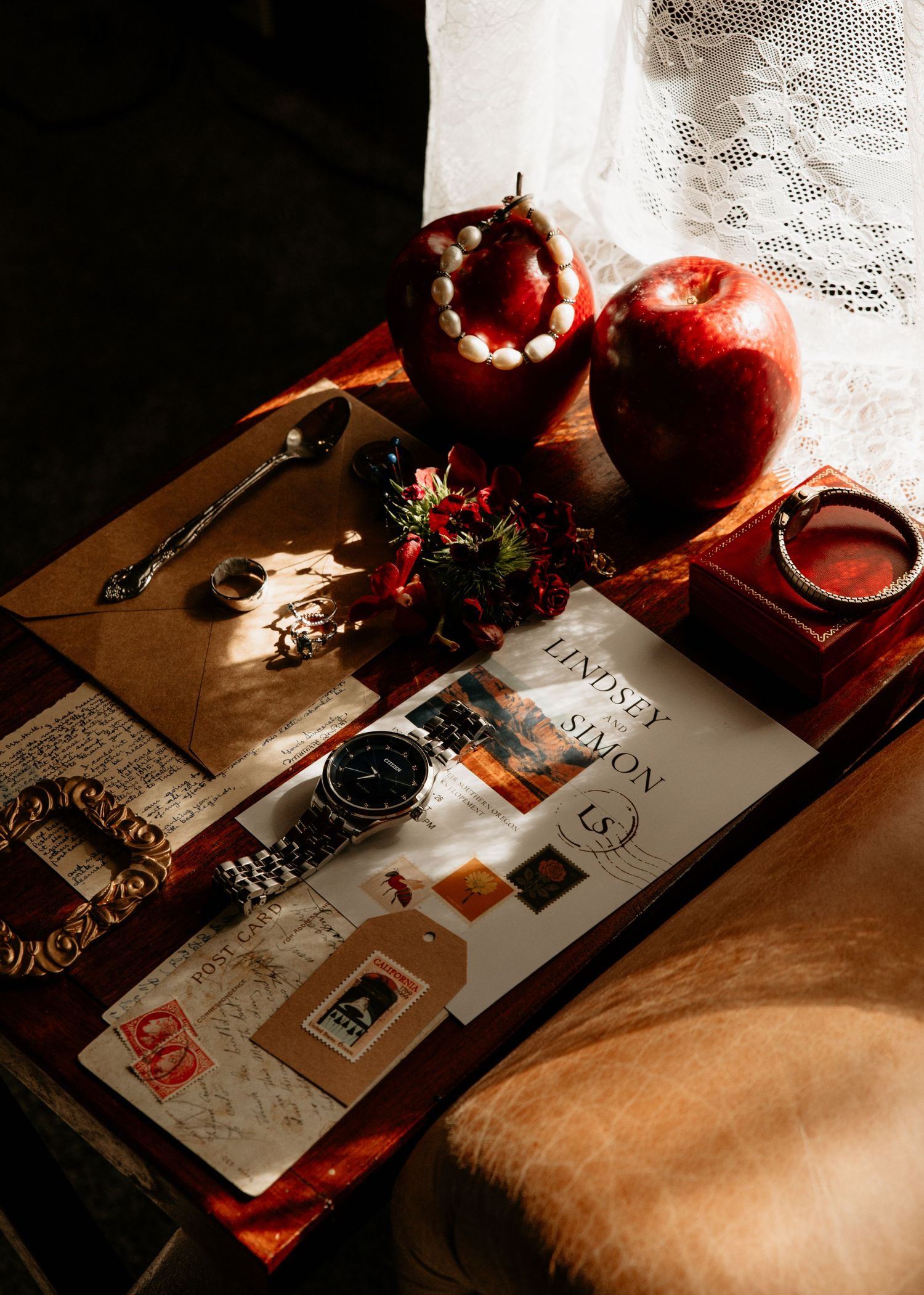 A vintage flat lay with a watch, apple, pearl bracelet, envelope, and flowers on a wooden tray in warm light.