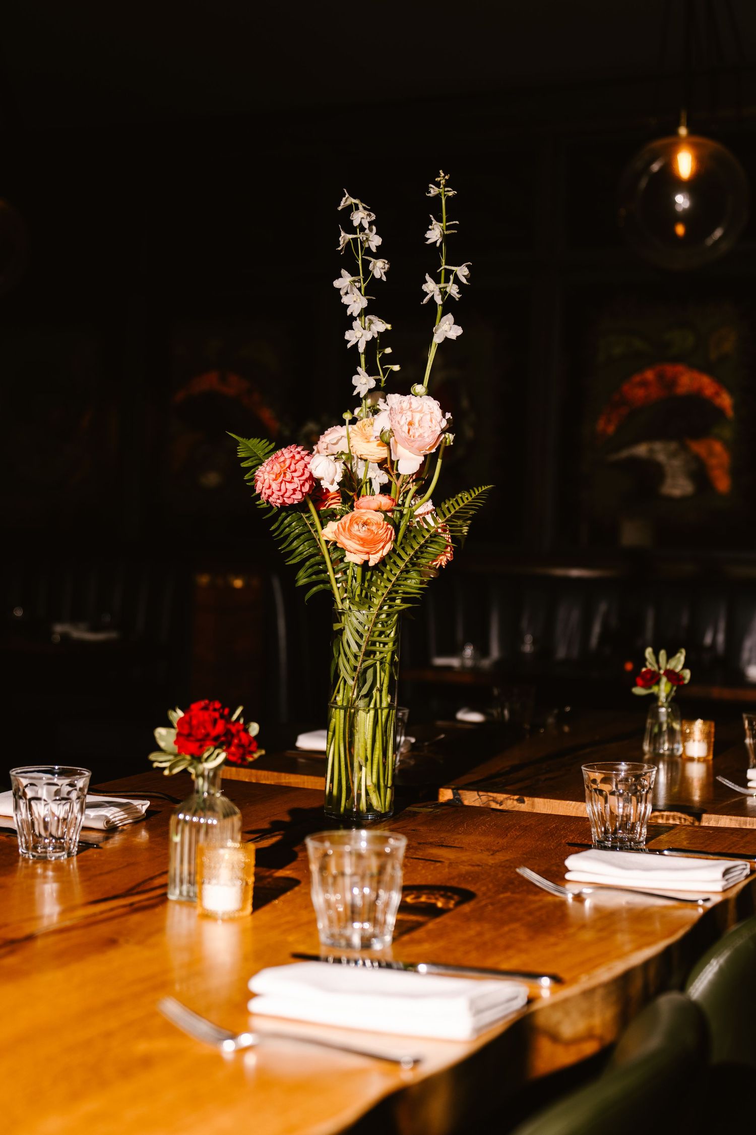 Elegant restaurant table with floral centerpiece featuring pink roses and white blooms on a warm wooden surface.