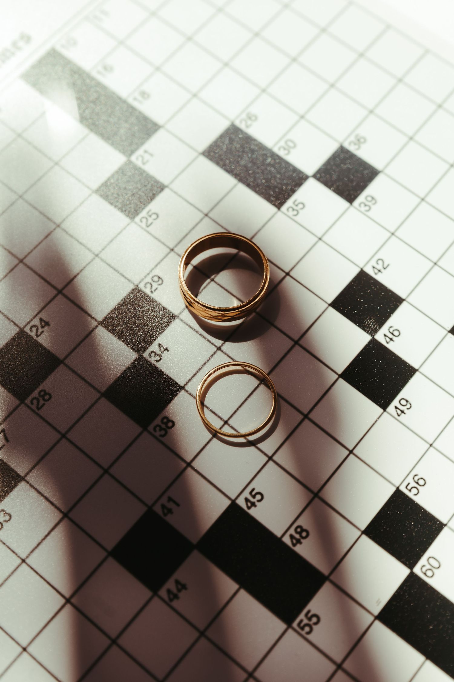 Two gold wedding rings resting on a crossword puzzle, symbolizing love and commitment.