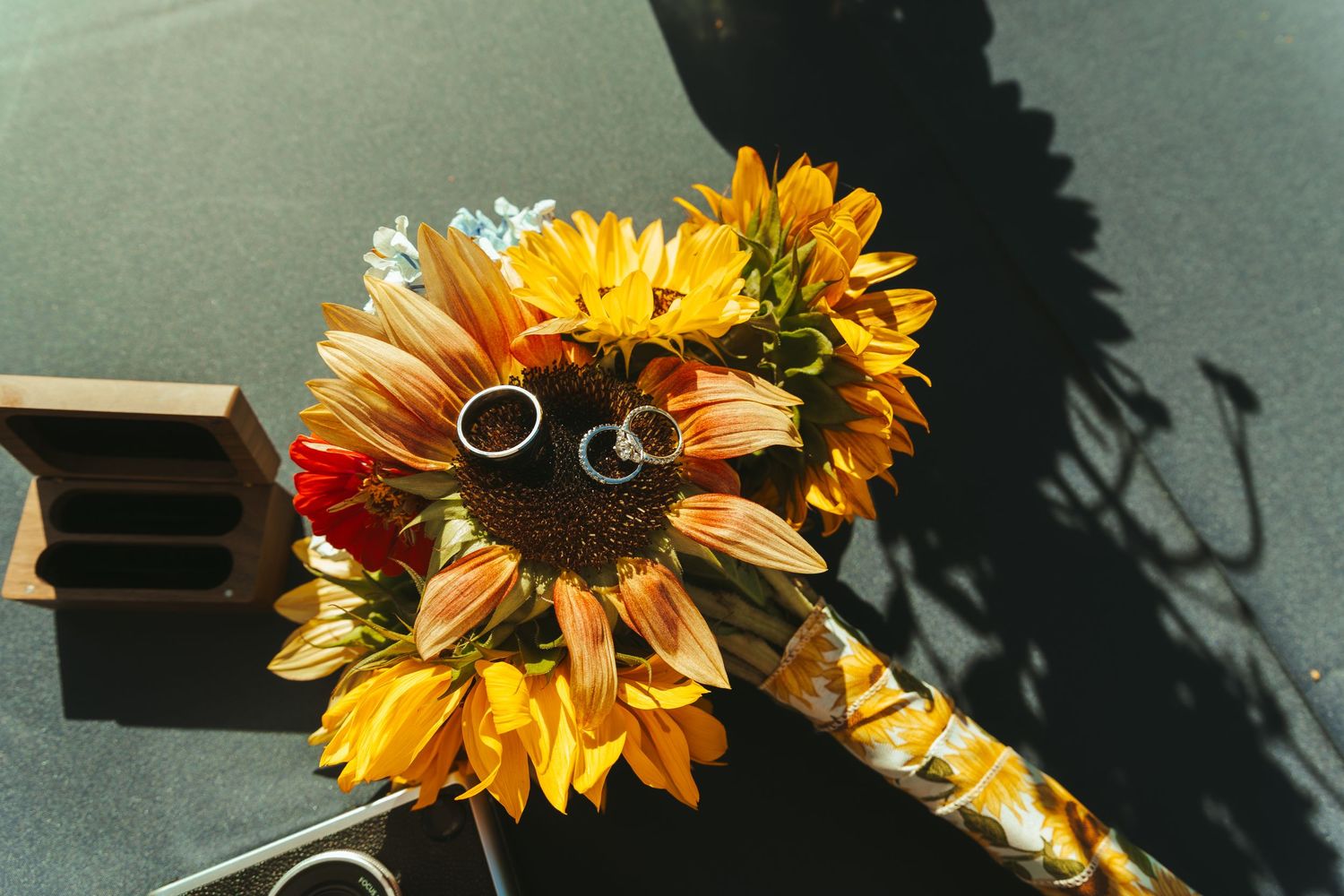Sunflower wedding bouquet with two gold rings resting on yellow blooms in bright sunlight.