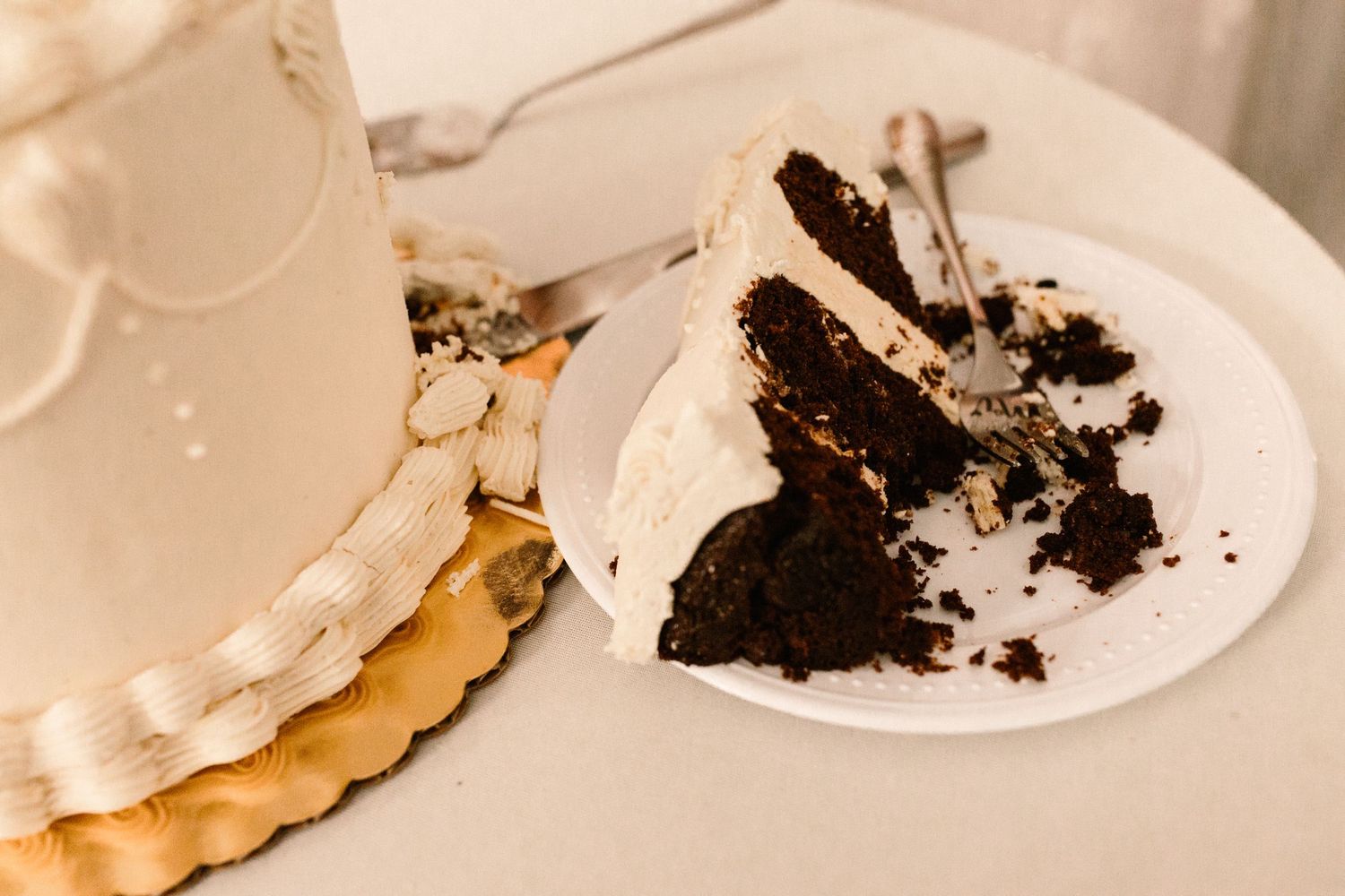 Slice of chocolate wedding cake with white frosting on a plate beside the tiered cake.