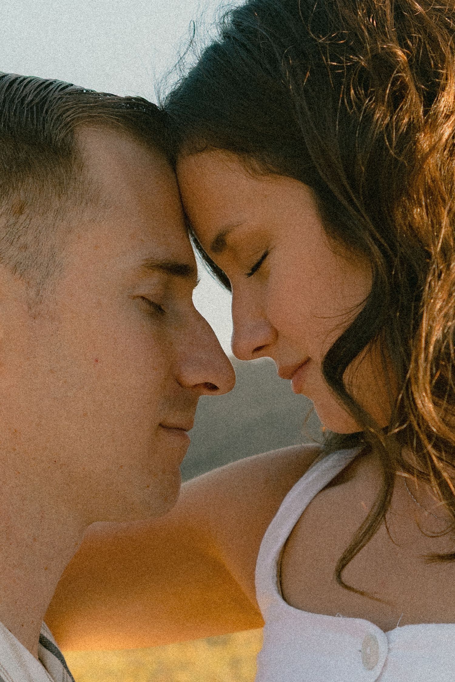 Romantic close-up portrait of a couple with foreheads touching against golden sunset light.