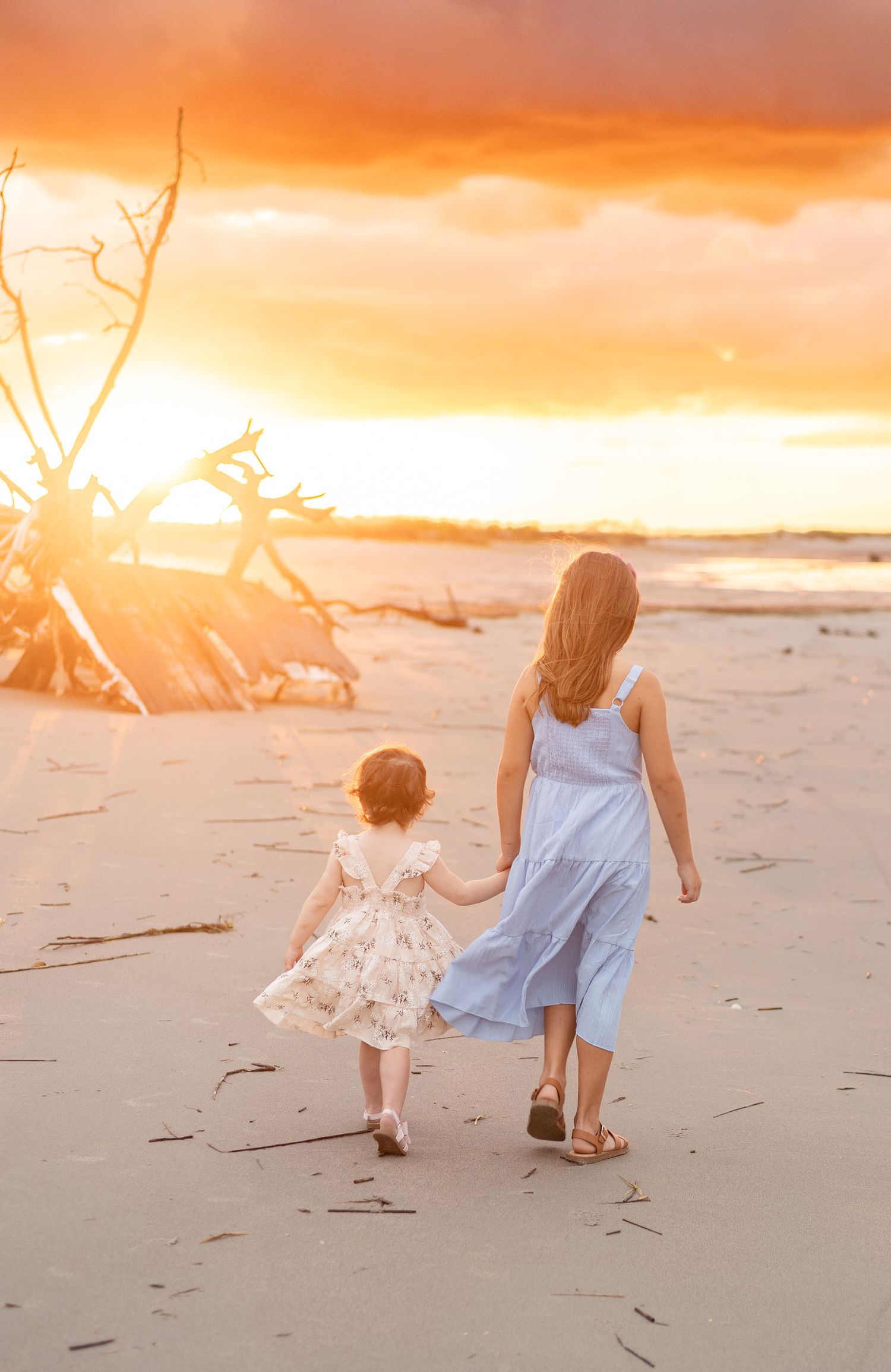 Two people walk along a sandy beach at sunset while holding hands and enjoying the warm golden light.