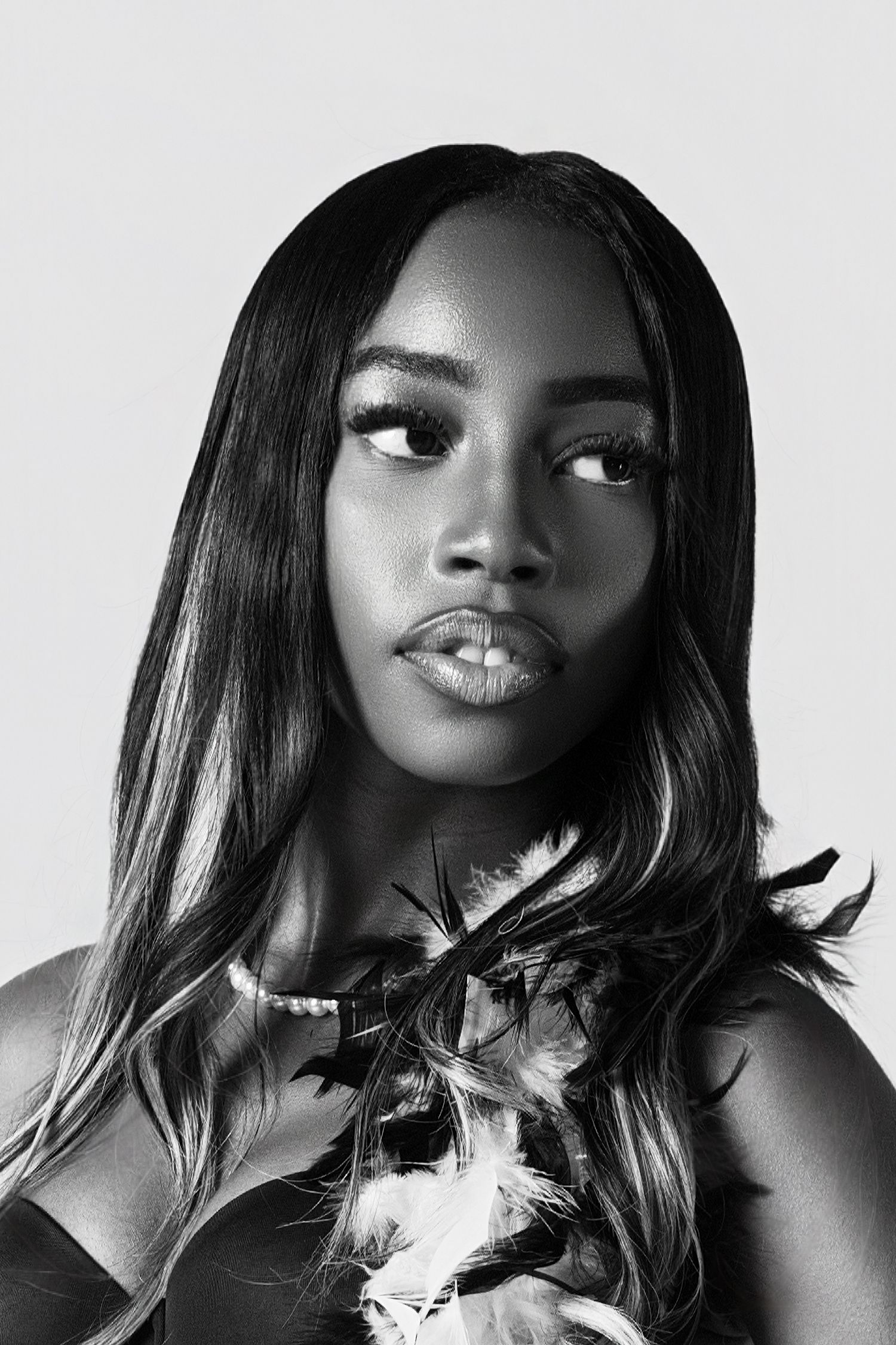 A striking black and white portrait of a model with long dark hair and feather accessories.