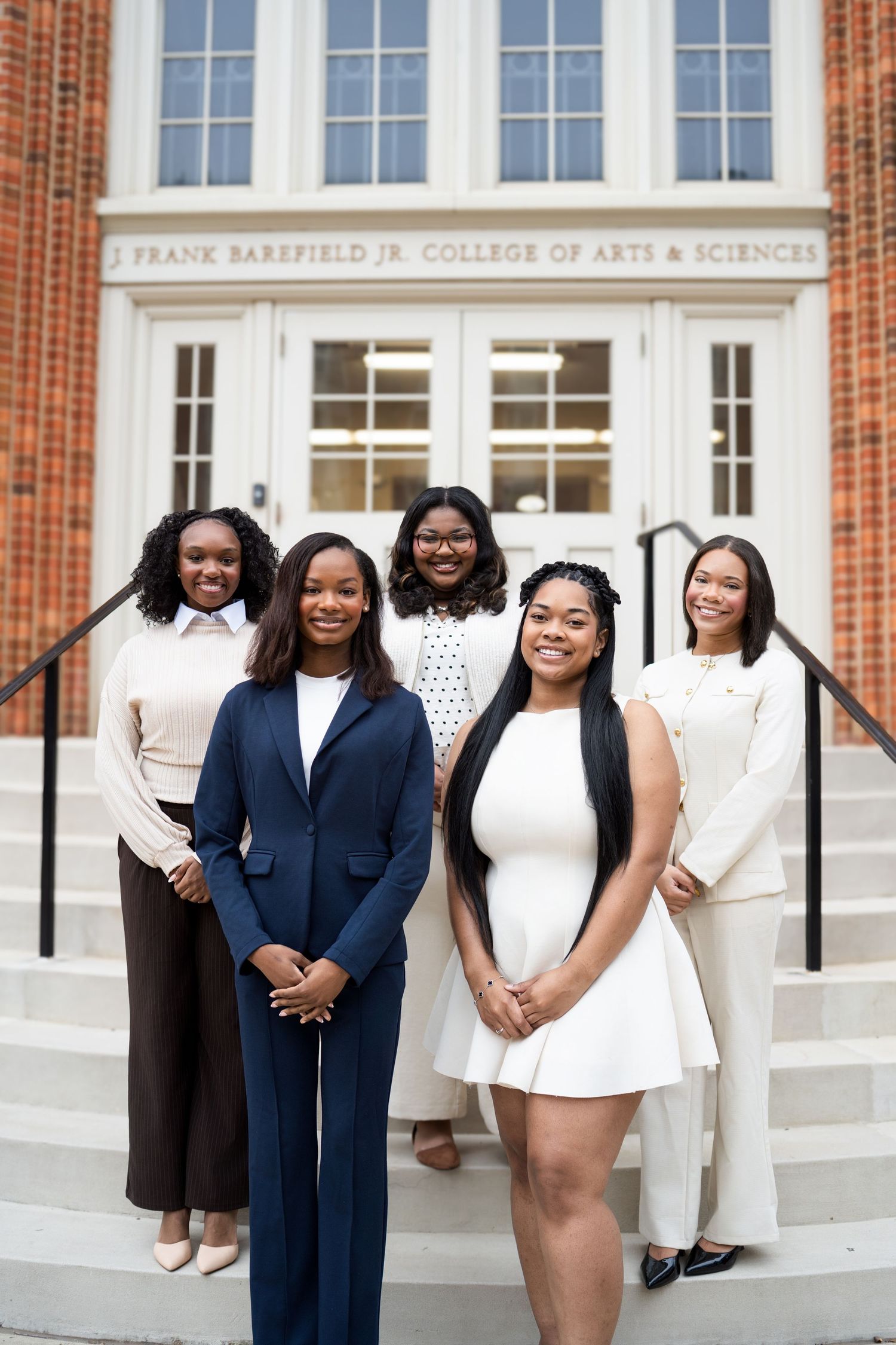 A group of students pose on the steps of the Frank Barkfield Jr. College of Arts & Sciences building.