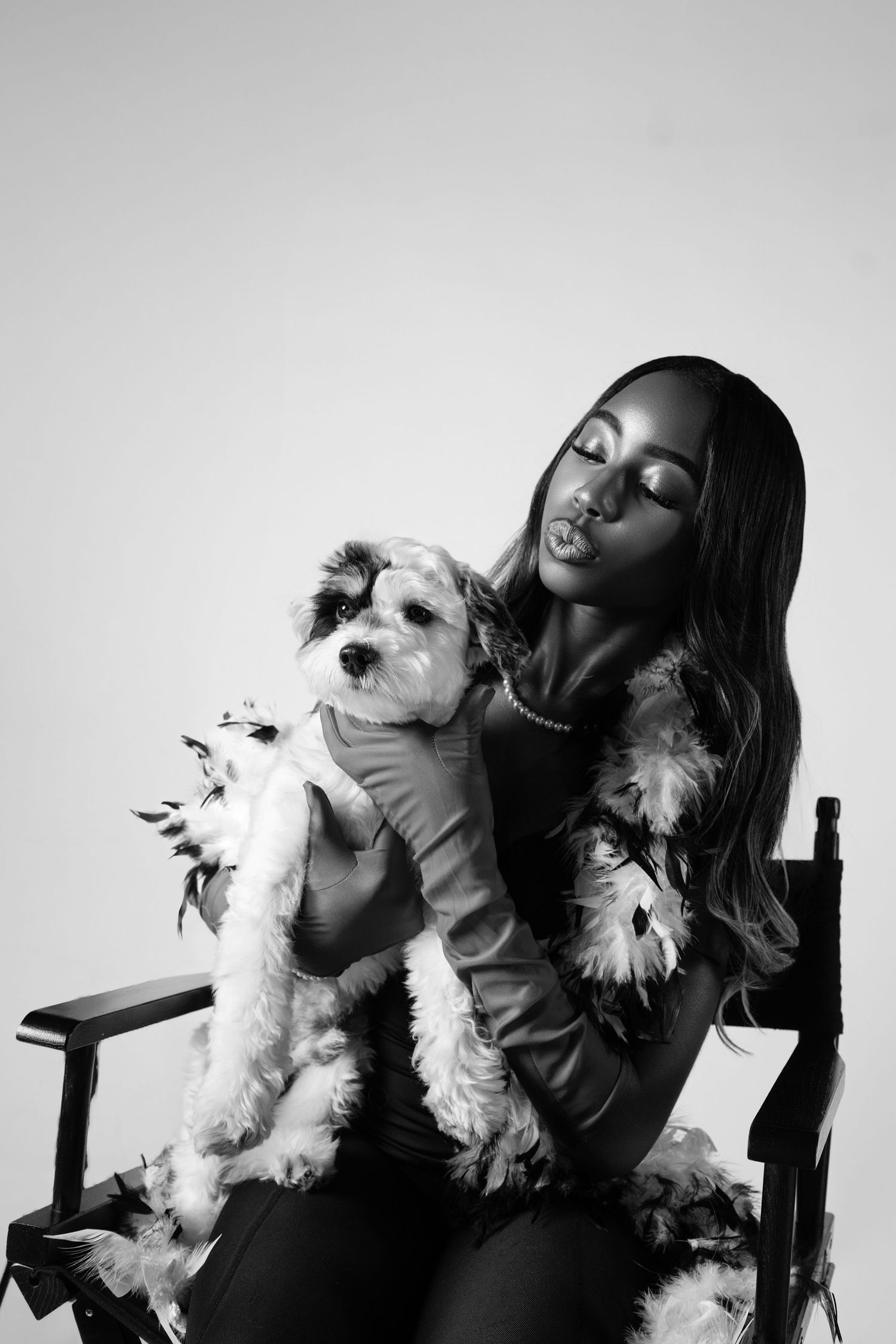 A person in black clothing poses affectionately with a small white fluffy dog in a series of black and white portraits.
