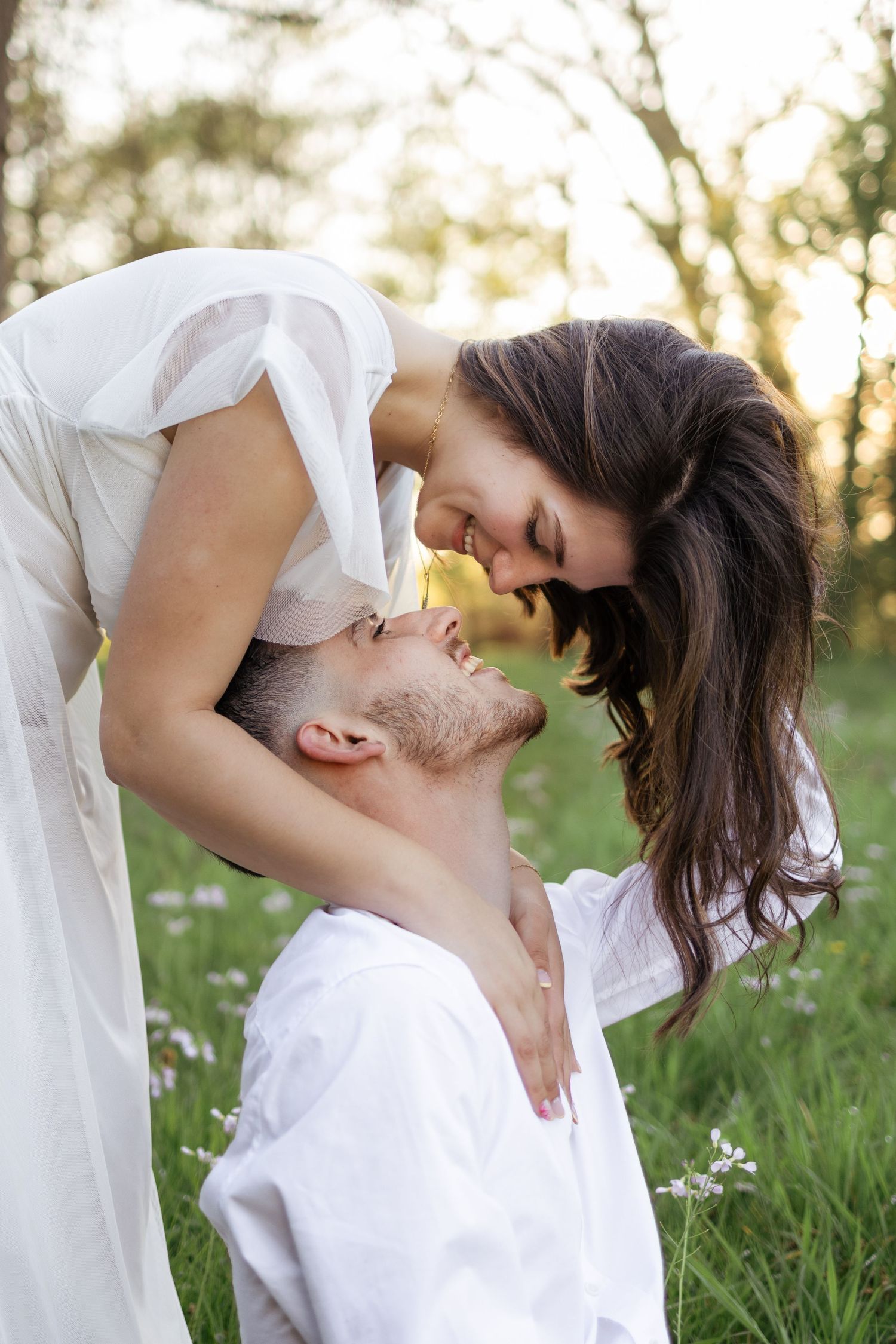 Romantic couple in white outfits sharing a tender moment in a sunlit flower field at golden hour.