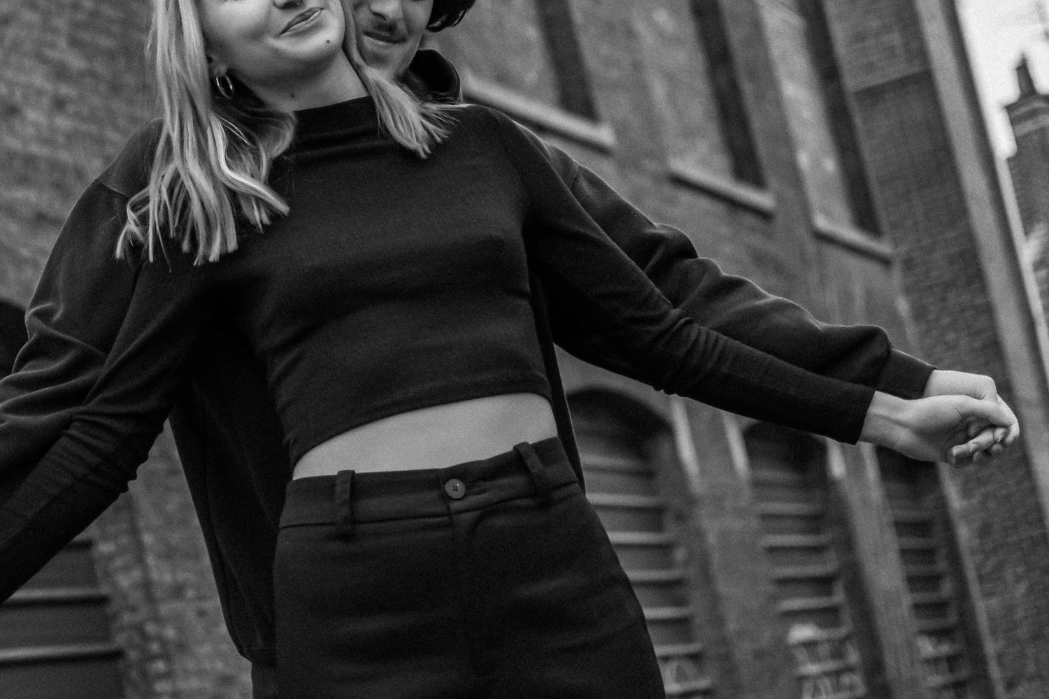 Black and white photo of a young blonde woman posing outdoors in a black crop top and high-waisted pants.