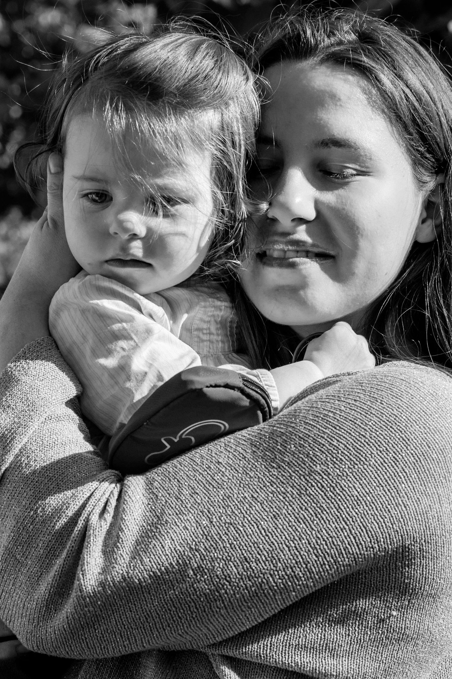 Black and white photo of a smiling woman tenderly holding a baby in her arms outdoors.