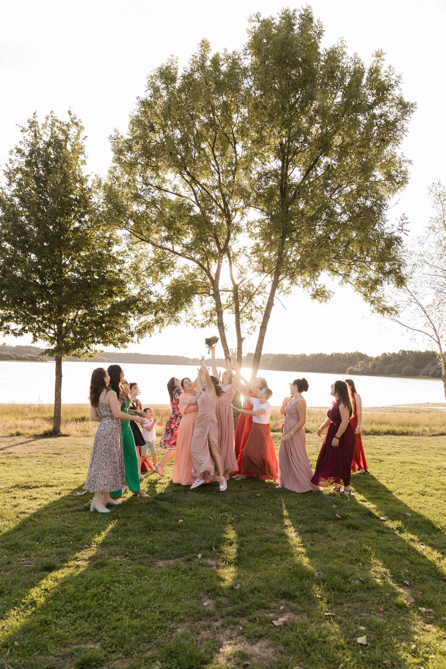 Group of women in colorful formal dresses celebrating outdoors near a lake at golden hour.