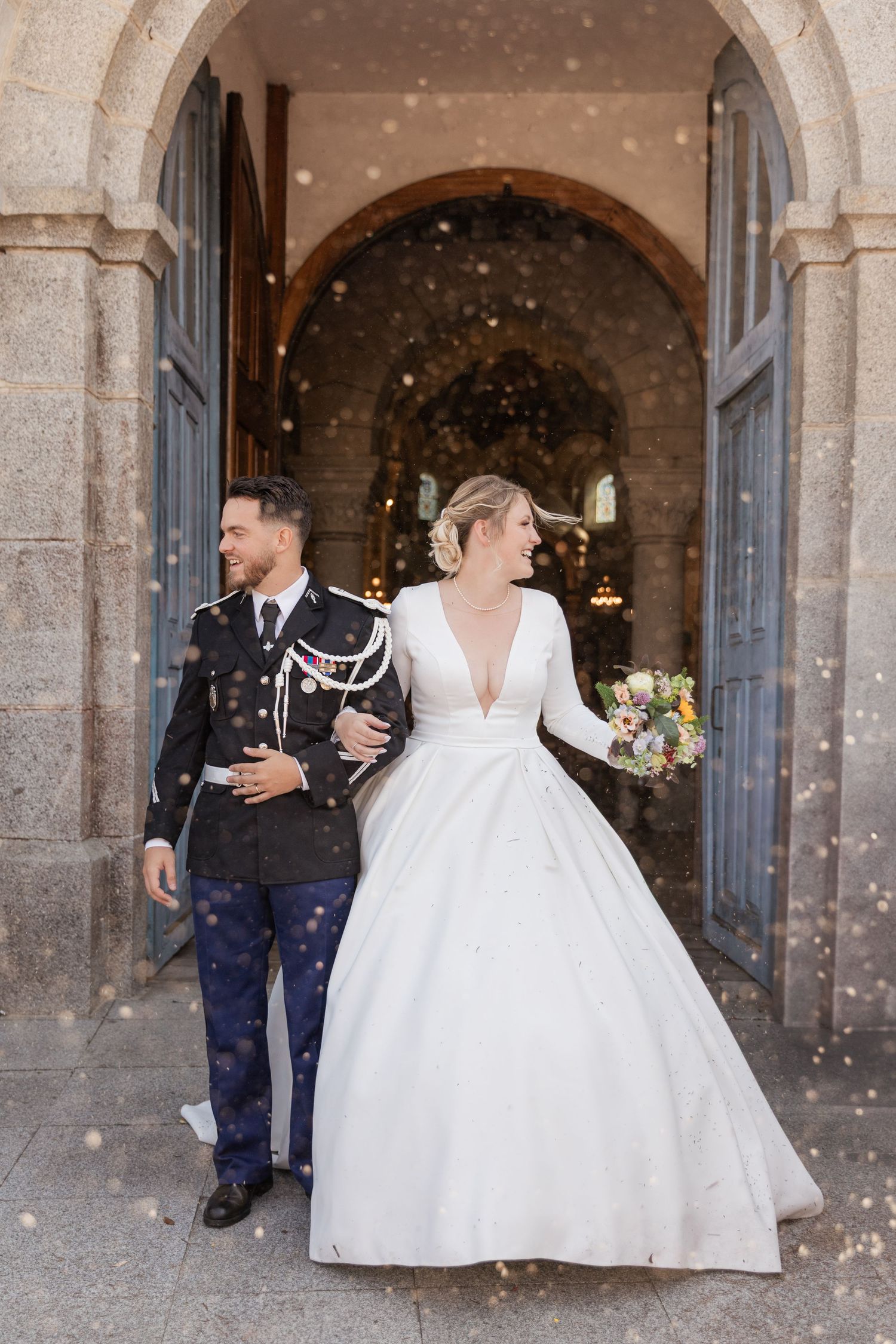 Bride and groom exit church in snowfall, she in white gown with bouquet, he in military dress uniform.