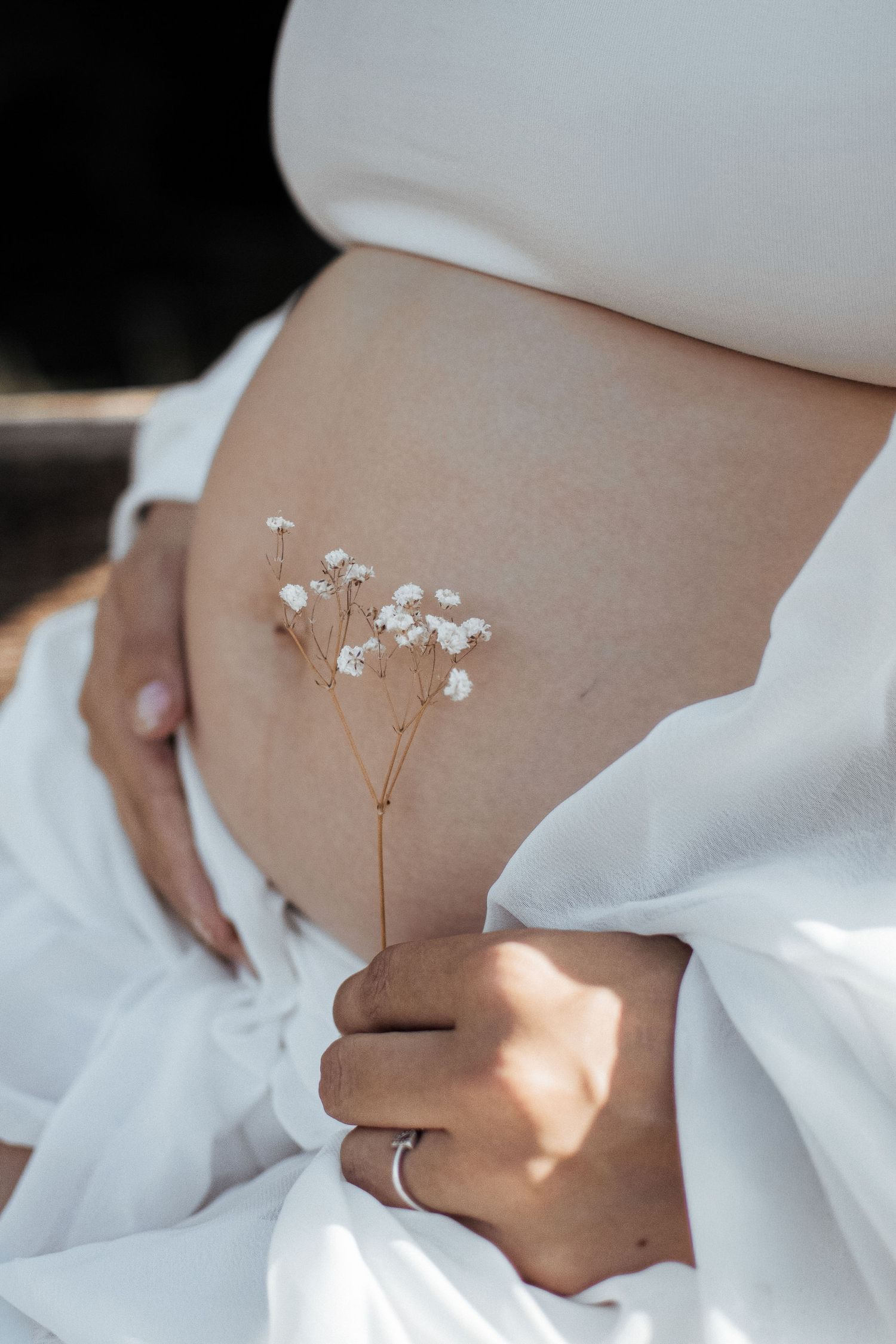 Pregnant woman in white dress holding delicate baby's breath flowers against her bare baby bump.