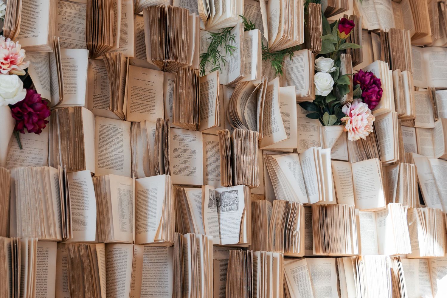 A decorative wall covered with open vintage books and colorful flowers including pink, red, and white blooms.