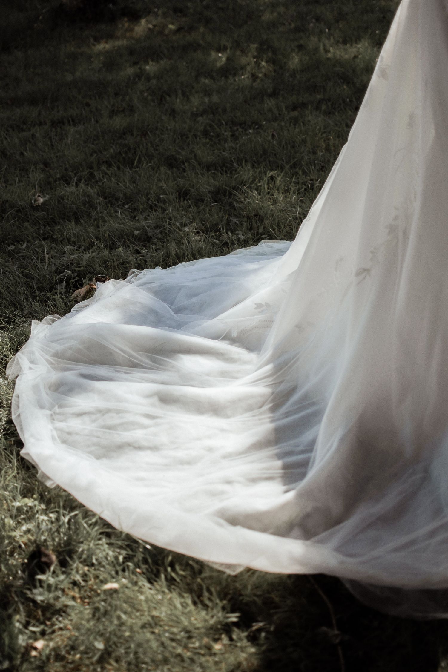 Elegant white wedding dress train spread on green grass outdoors.