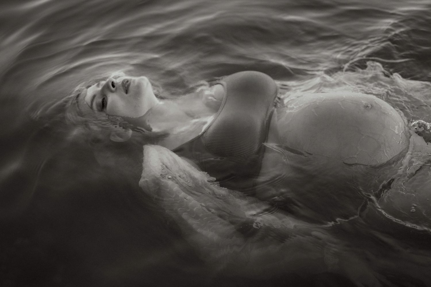 Black and white photo of a woman pregnant floating in water wearing a bikini top.