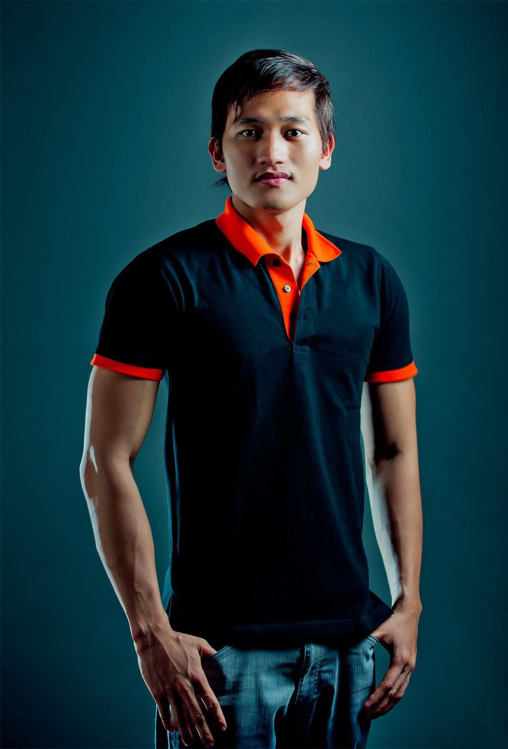 Portrait of person in black and orange polo shirt against teal background.