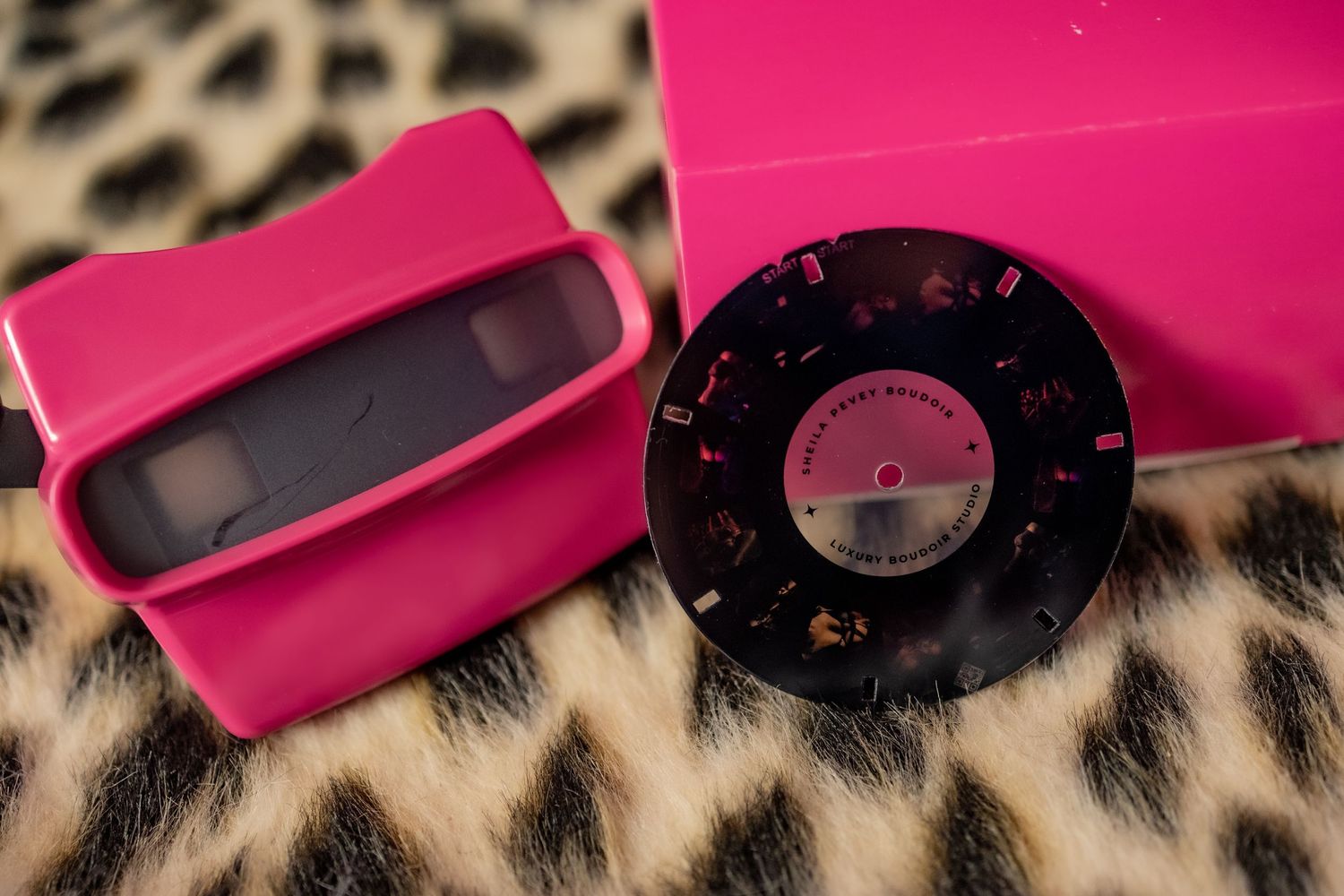 A pink vintage View-Master 3D viewer and reel displayed on a leopard print background.