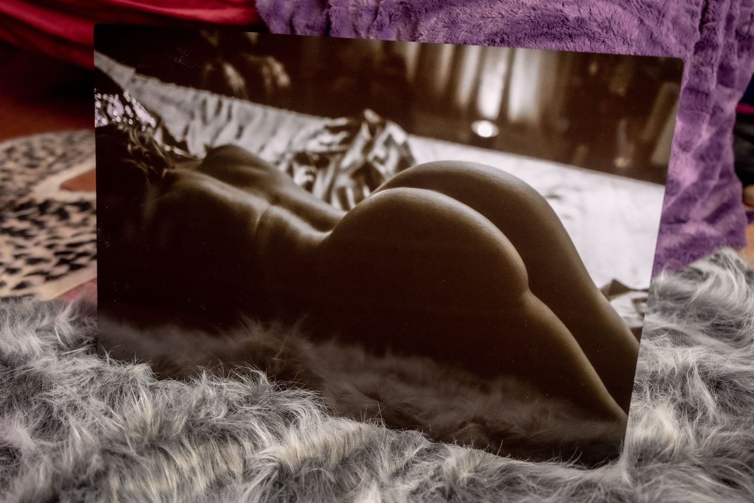 A black and white artistic nude photograph laid on purple fabric showcases gentle curves and shadows.