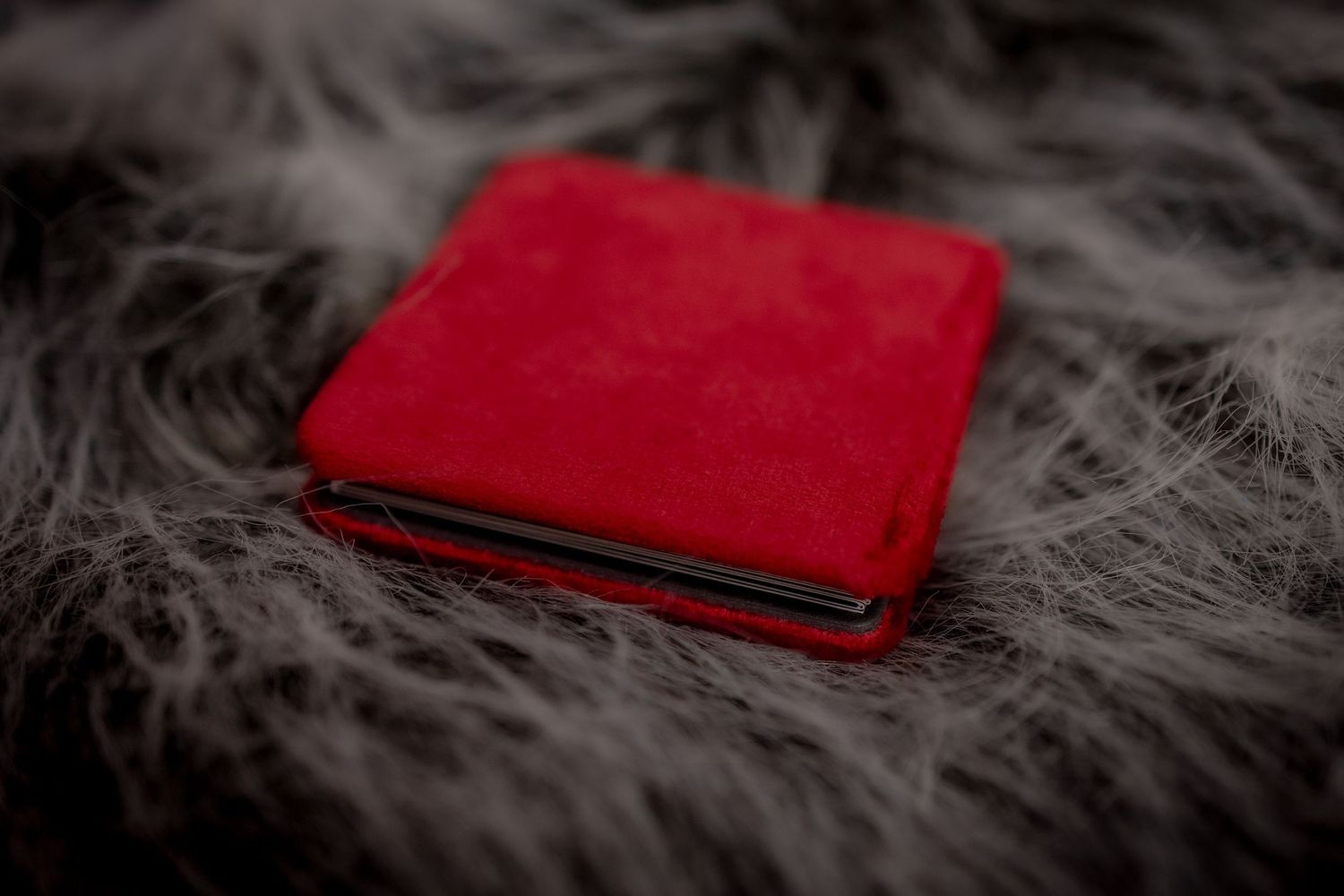 A bright red leather boudoir photo album sits on a soft gray fur or fuzzy textured surface.