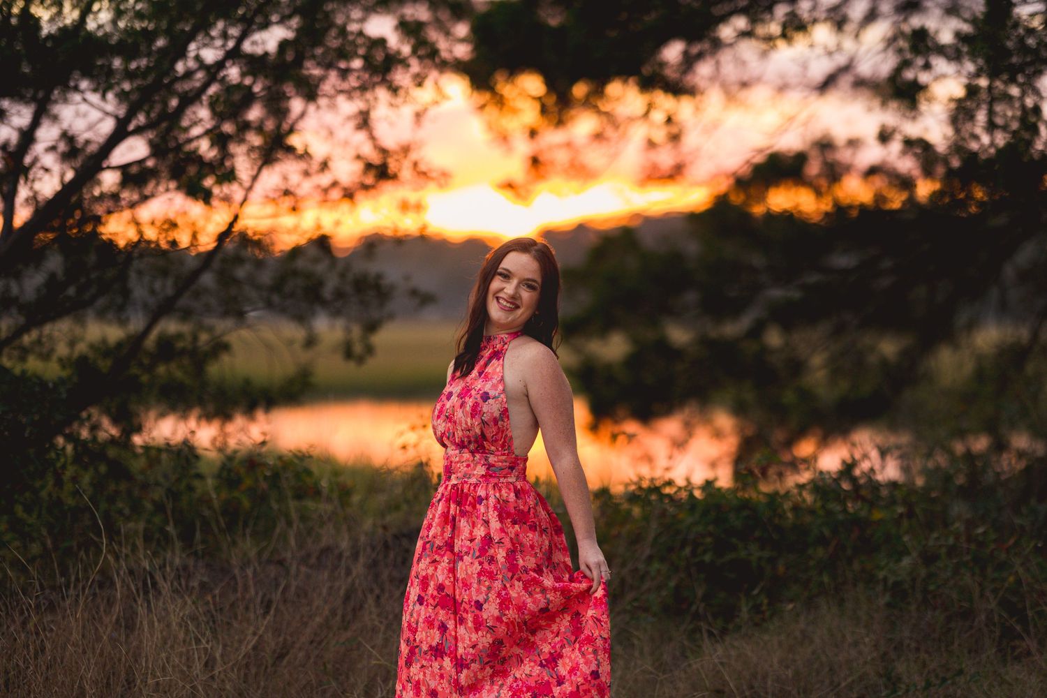 Red floral dress captures movement against a glowing sunset by a serene lake.