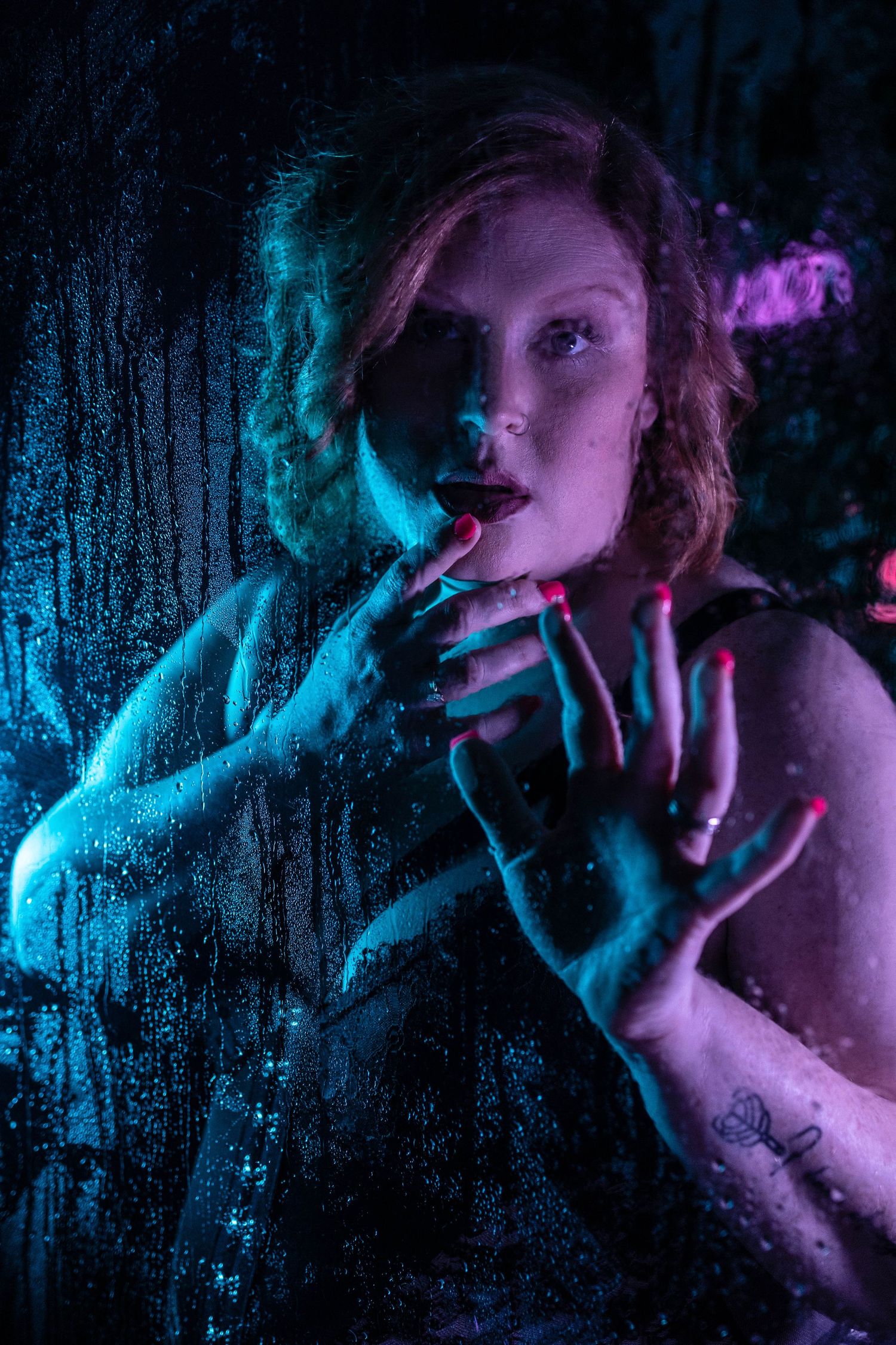 Artistic boudoir portrait with neon blue and purple lighting against wet shower glass creating a moody atmosphere.