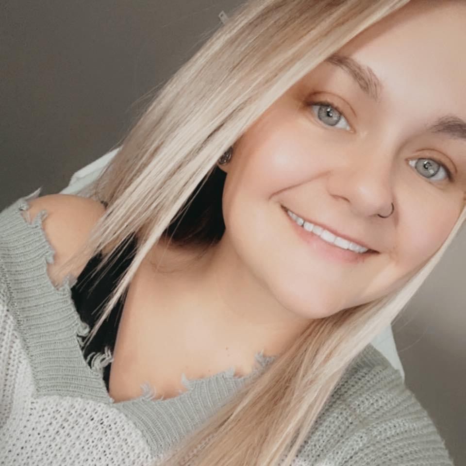 Smiling person with platinum blonde hair wearing a light gray sweater in a close-up selfie portrait.