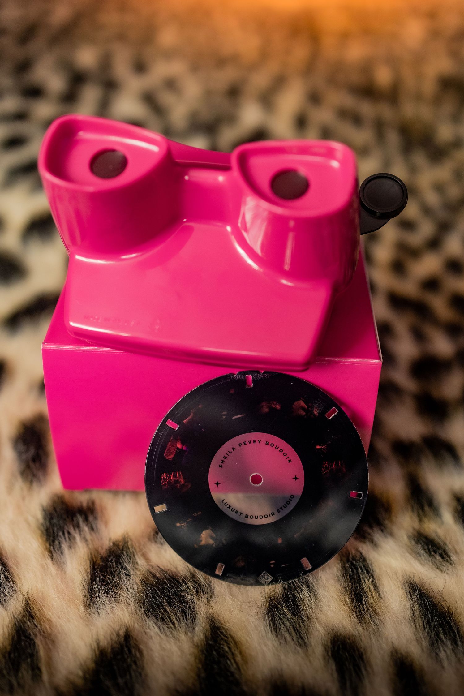 Pink vintage Boudoir View-Master toy photographed on leopard print fabric with a black reel disc visible.