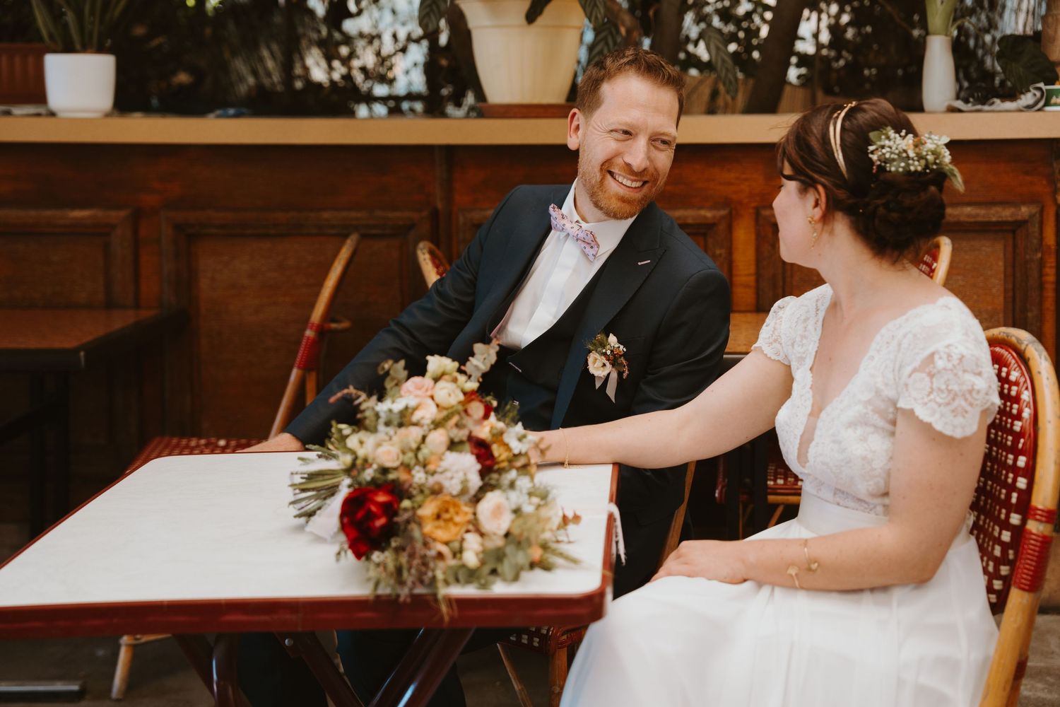 Un couple en tenue de mariage assis ensemble à une table en bois lors de leur réception. Reportage de mariage vivant et authentique