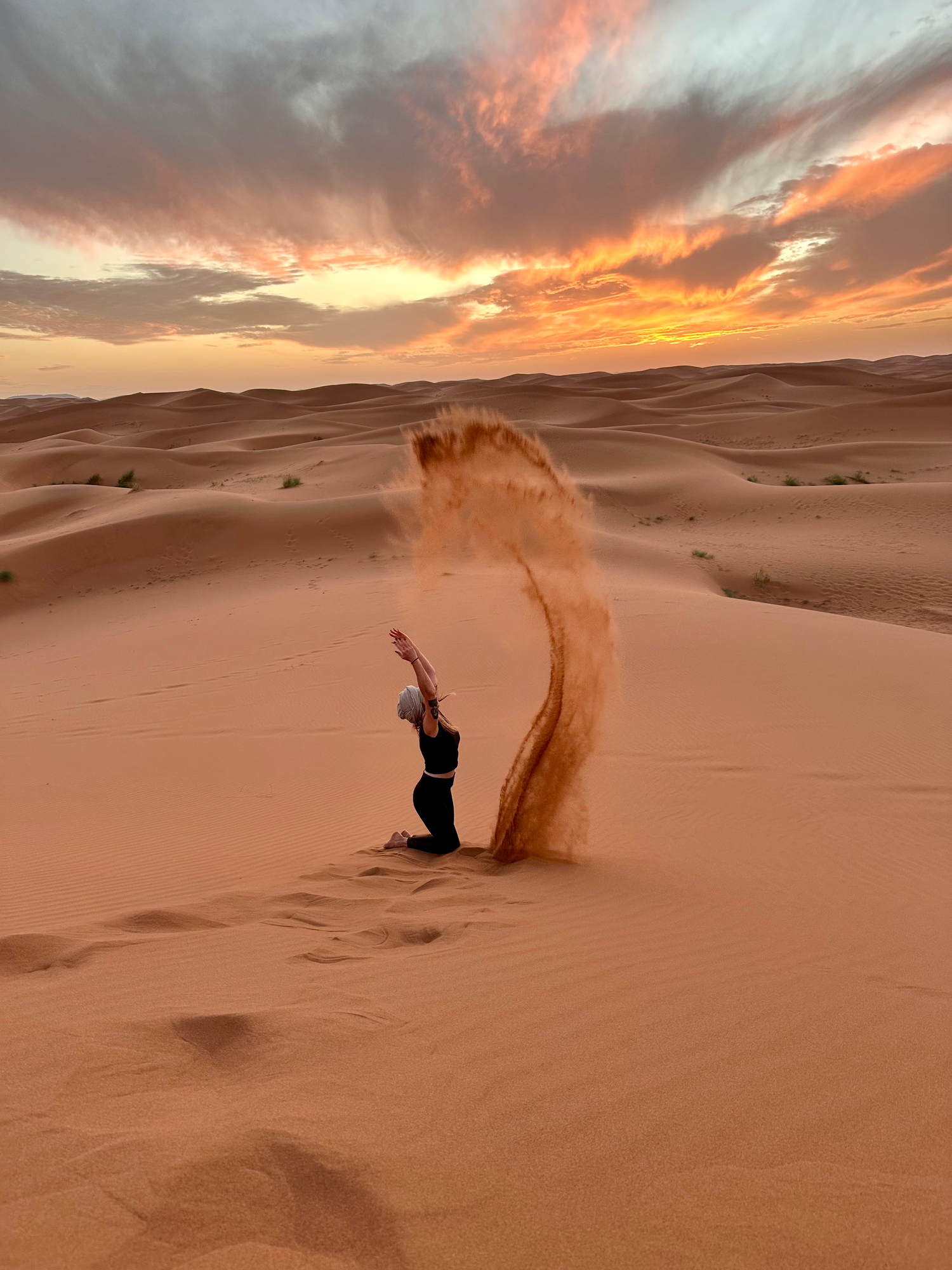 Figure creating dramatic sand cloud in desert landscape during golden hour sunset.