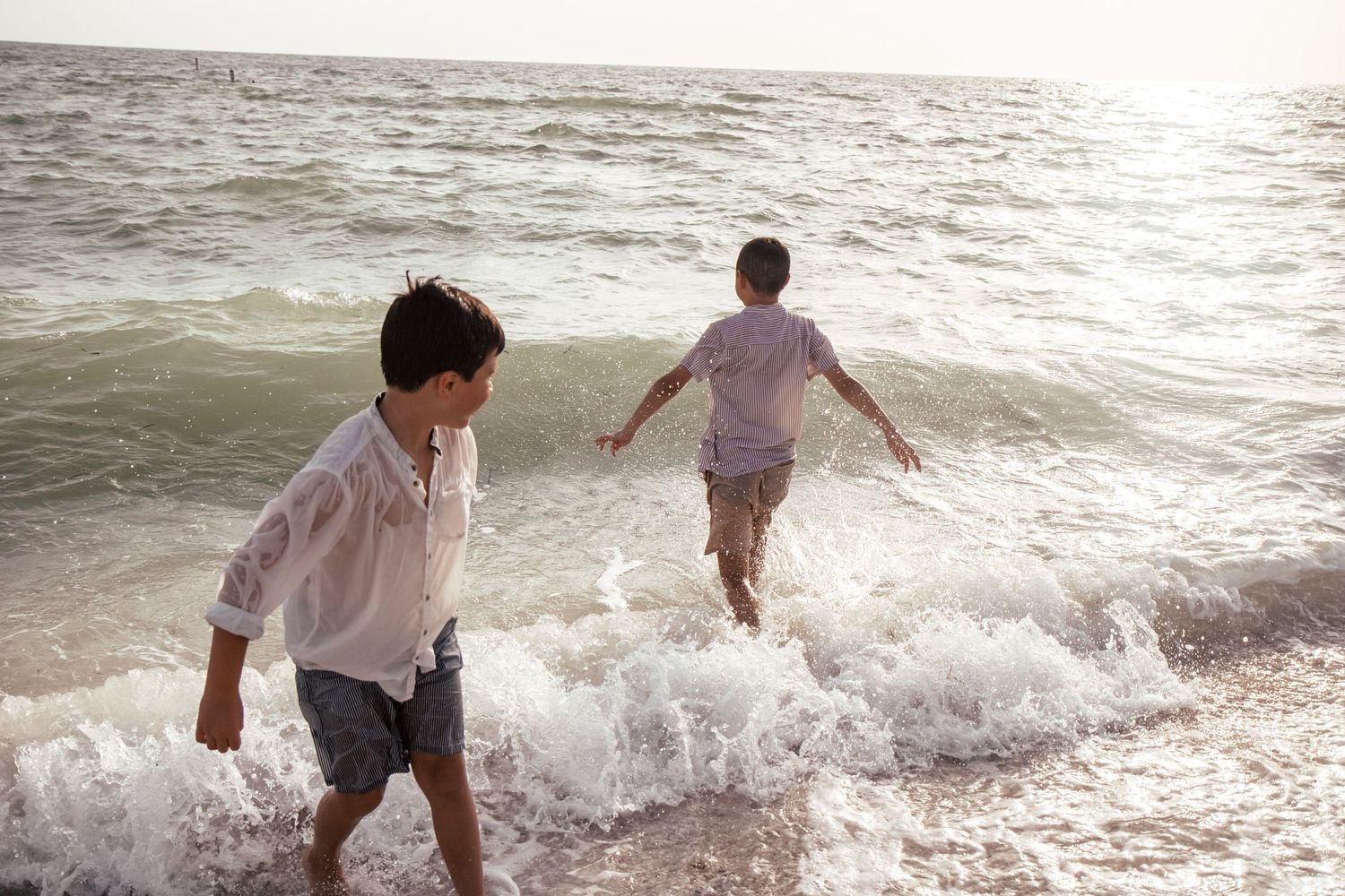 Two boys playing in ocean waves while dressed in formal clothes during a beach photo session
