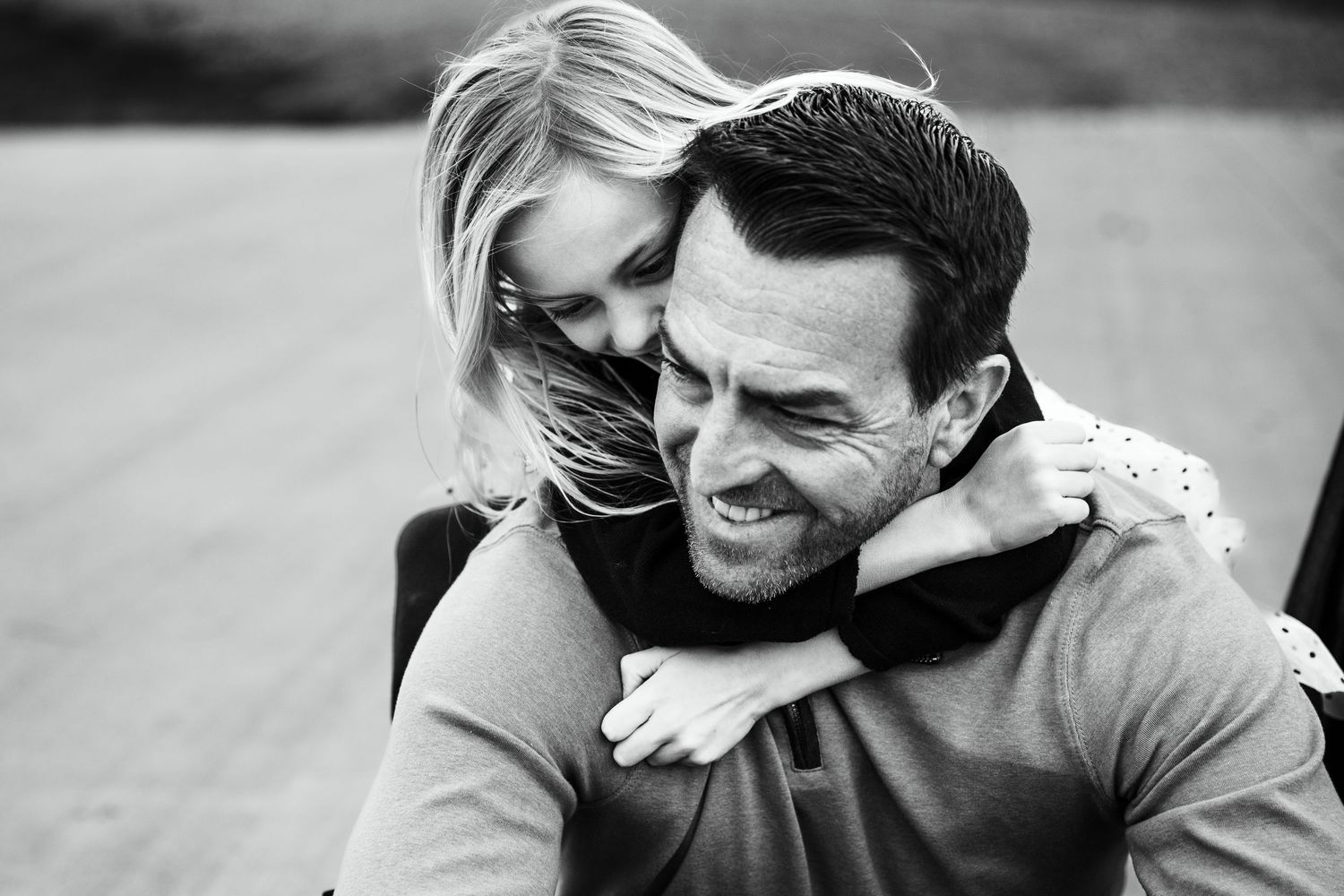 Black and white photo of a smiling couple, woman hugging man from behind outdoors.